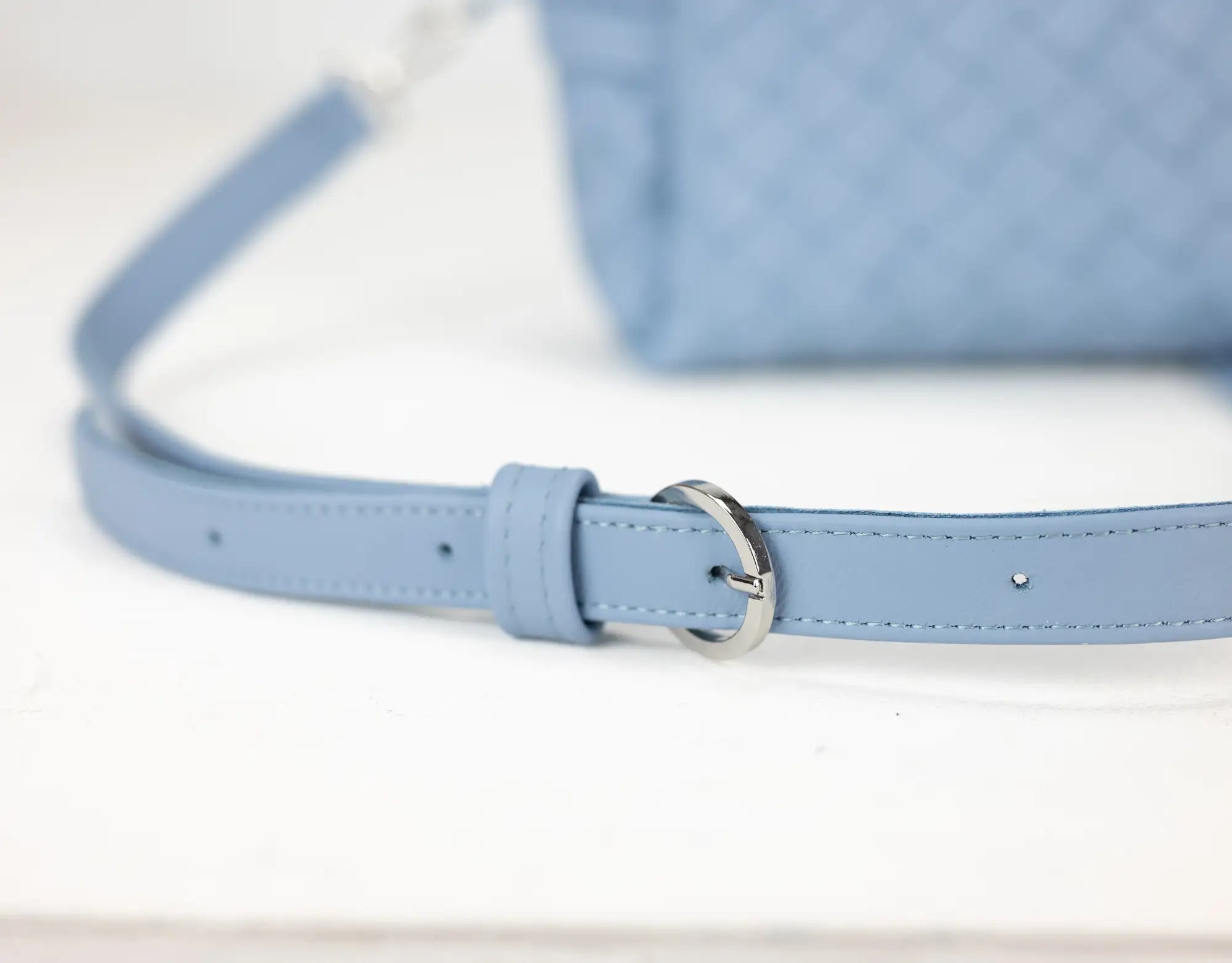 Close-up of a light blue leather belt with a silver buckle on a white background