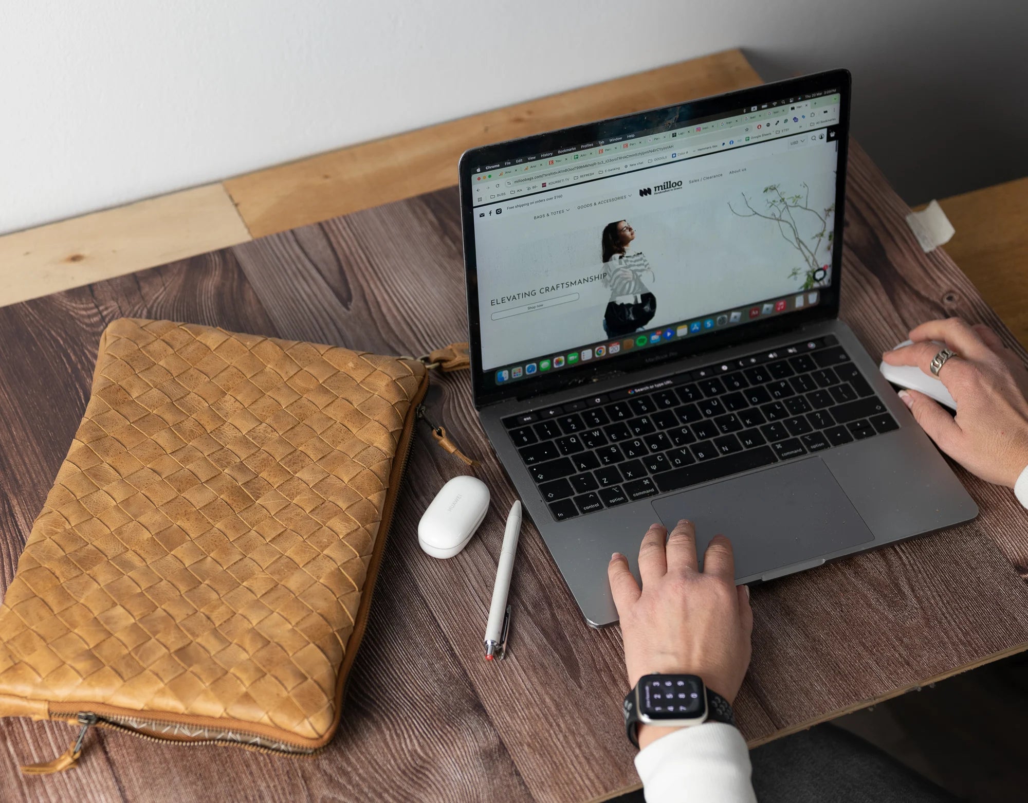 Person using a laptop on a wooden desk with a brown leather pouch and white mouse.
