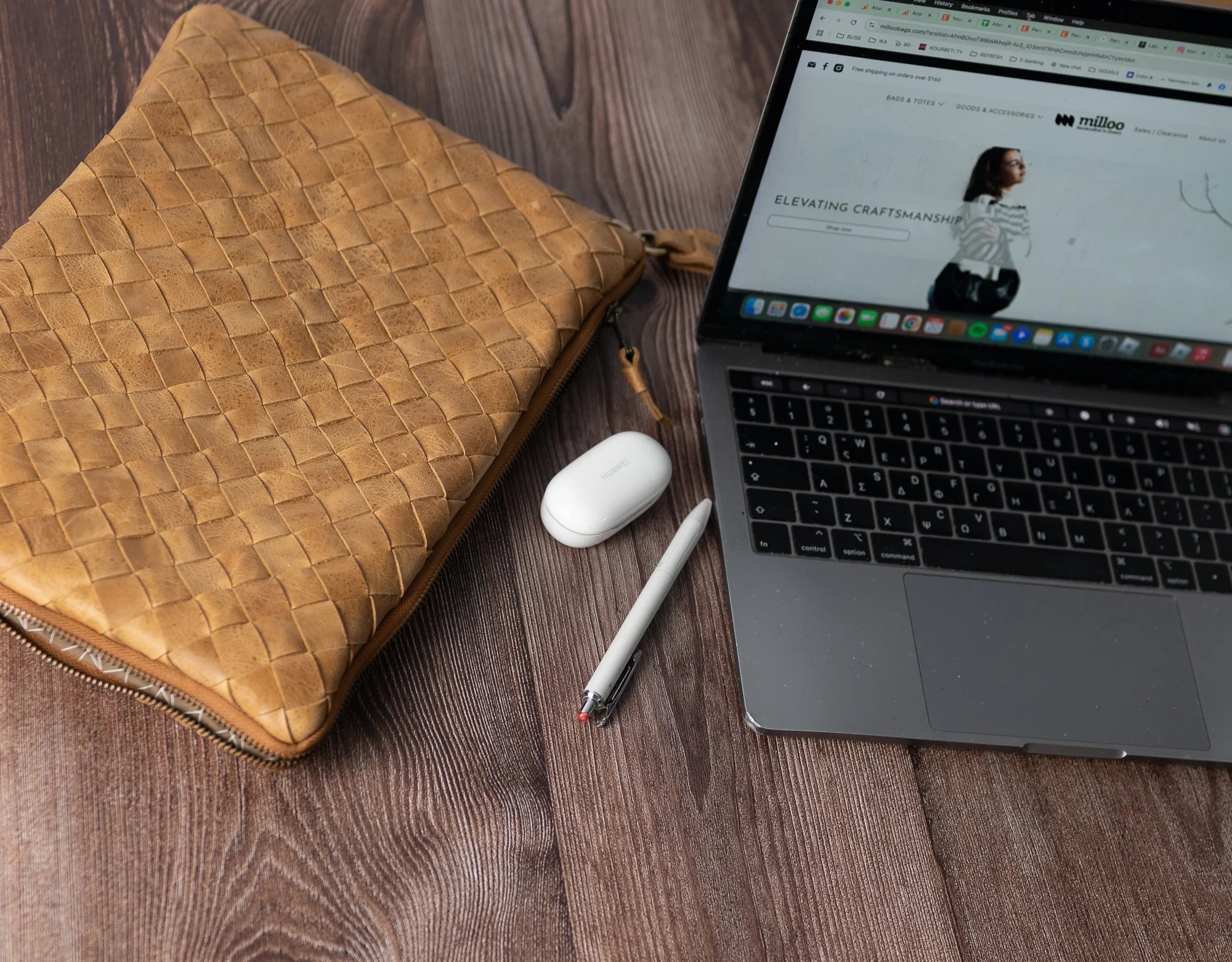 Laptop on a wooden surface with a woven brown pouch, white mouse, and pen.
