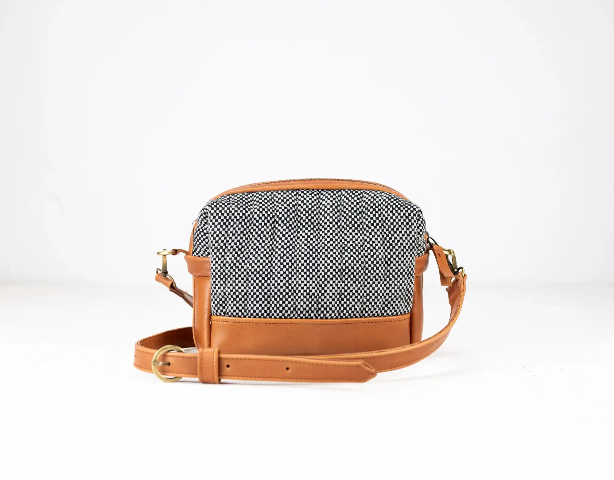 Handbag with herringbone pattern and brown leather strap on a white background