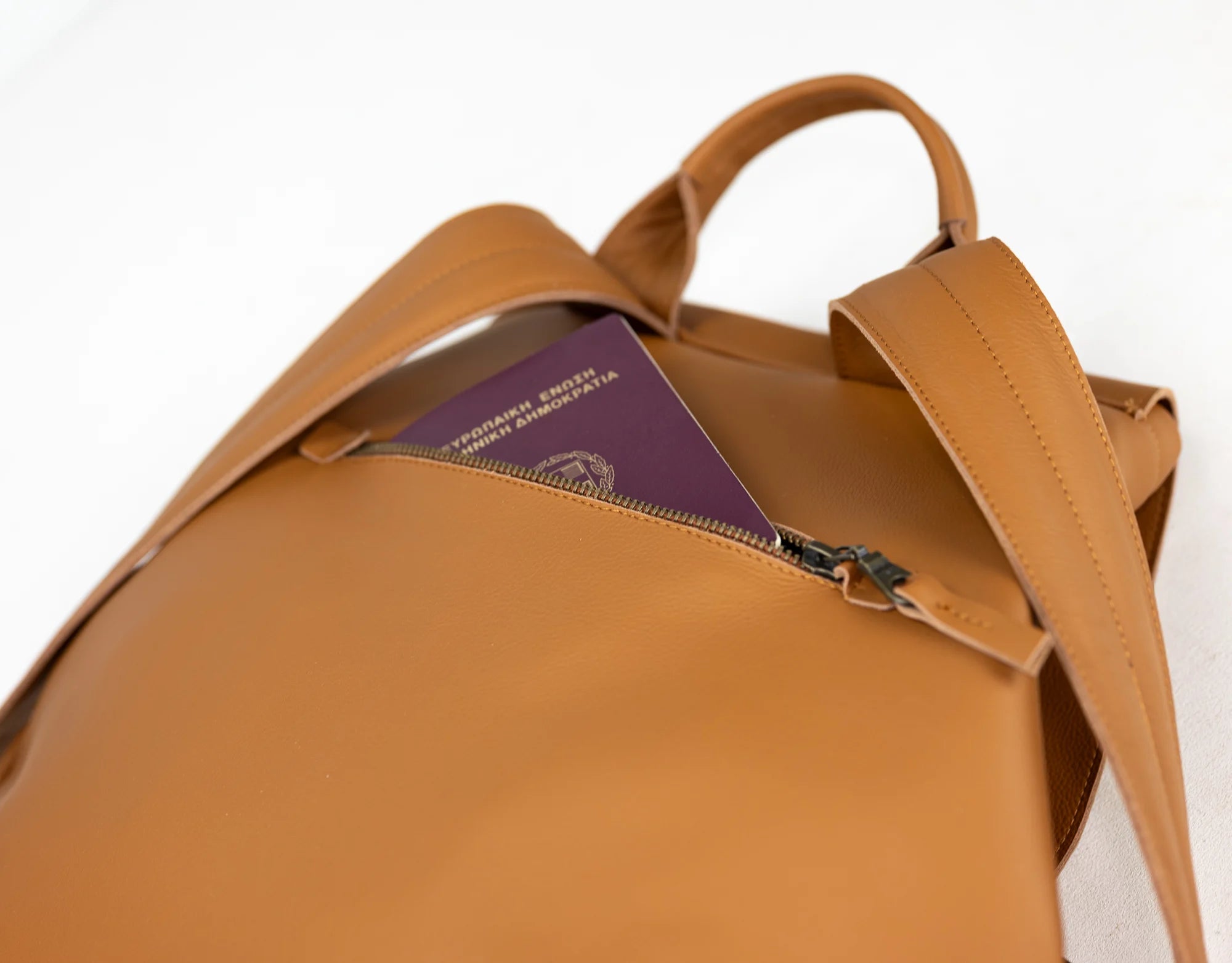 Brown leather backpack with a passport in the front pocket on a white background