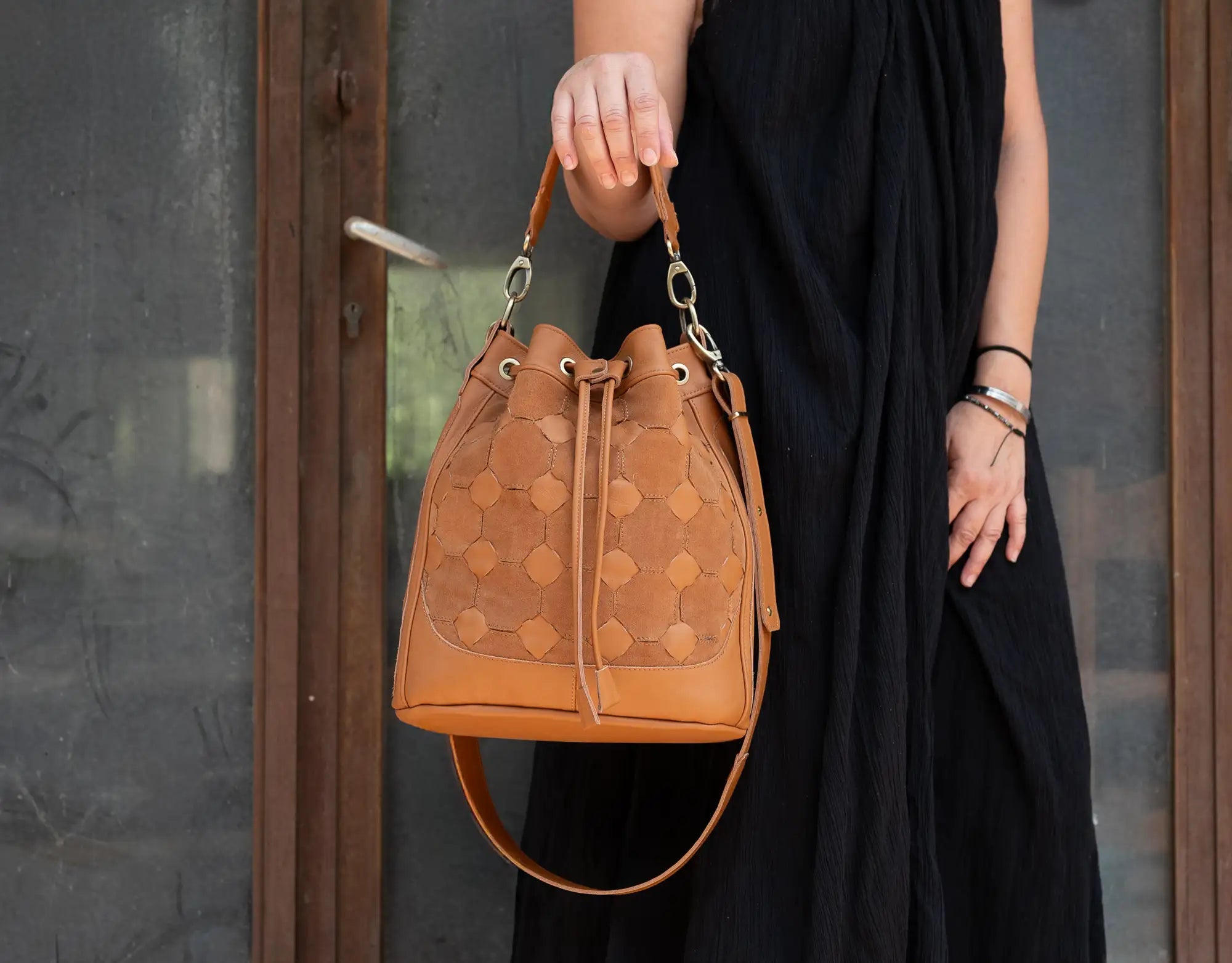 Person holding a brown leather handbag with a patterned design against a neutral background