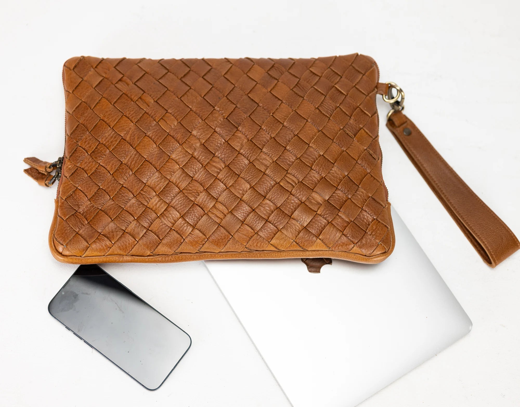 Brown woven clutch bag with a phone and laptop on a white background