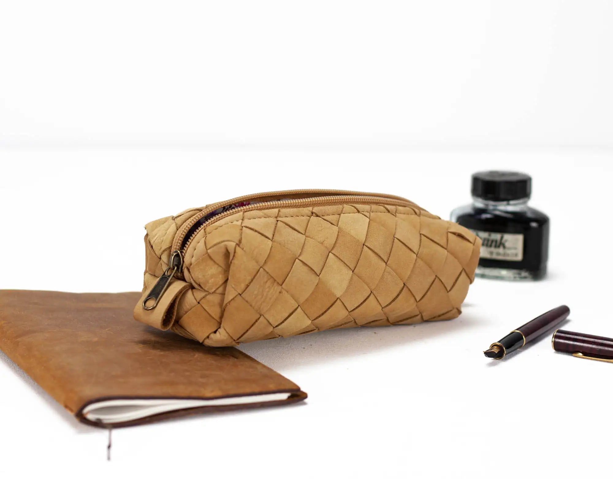 Brown woven pouch, notebook, and ink bottle on a white background
