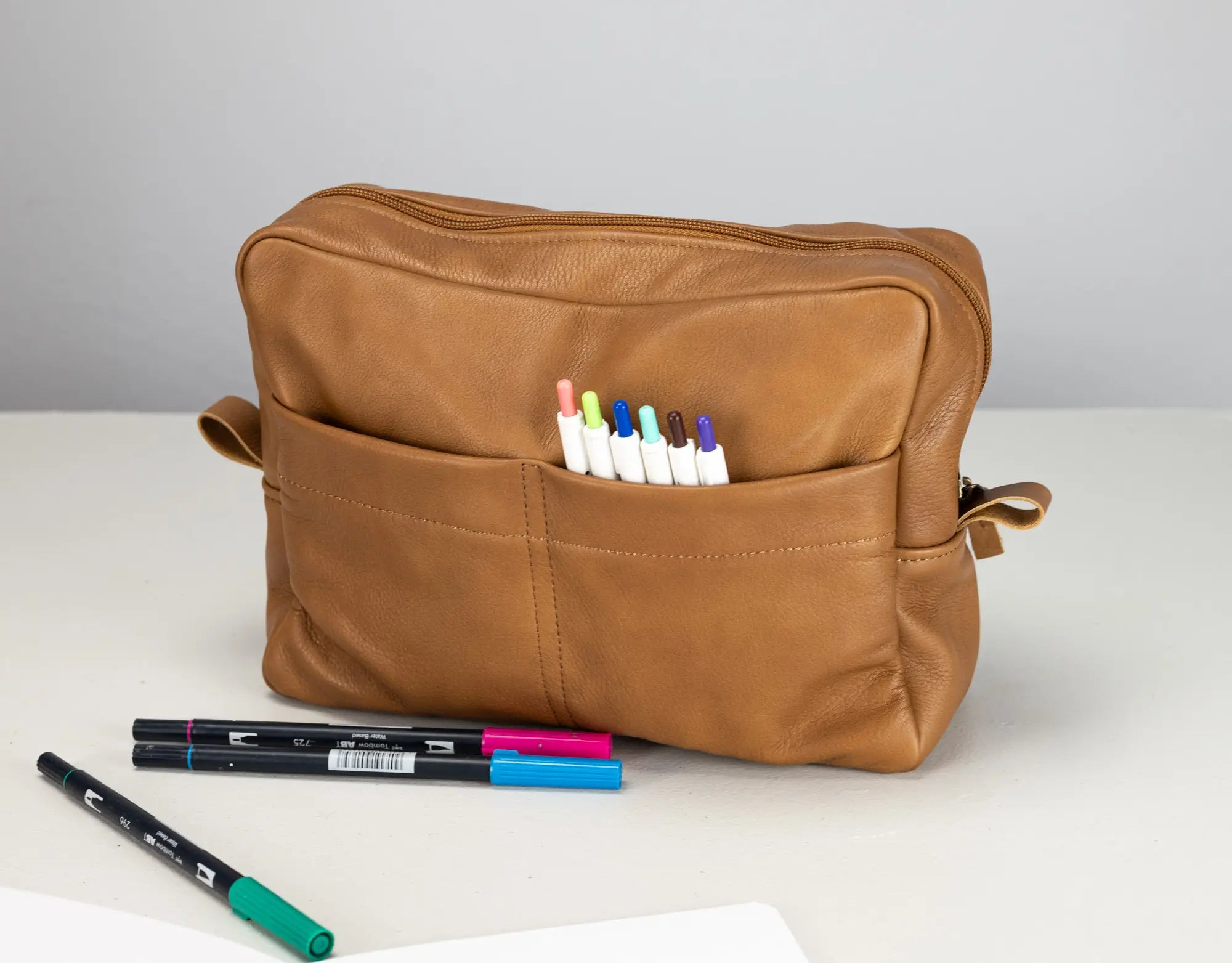Brown leather pouch with markers on a white surface