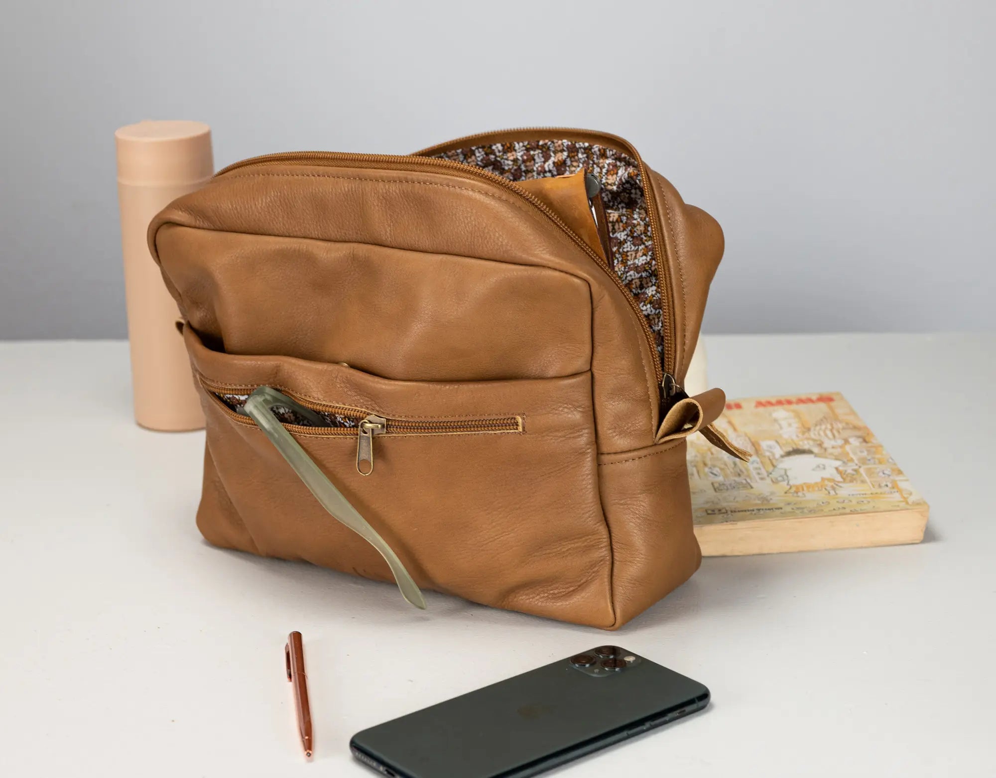 Brown leather bag with items like a phone and pen on a light surface.