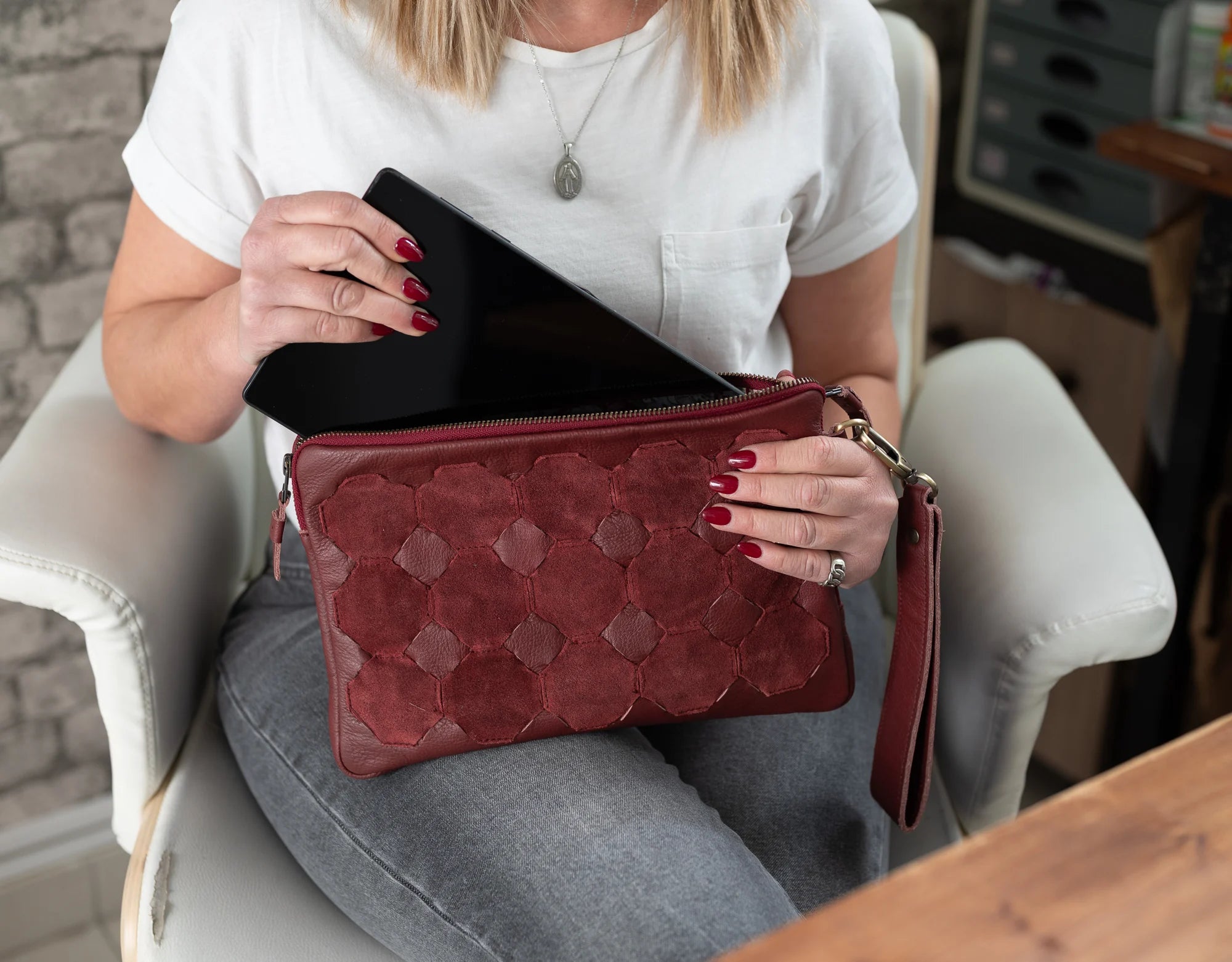 Woman sitting in a chair holding a red clutch bag with a brick wall background