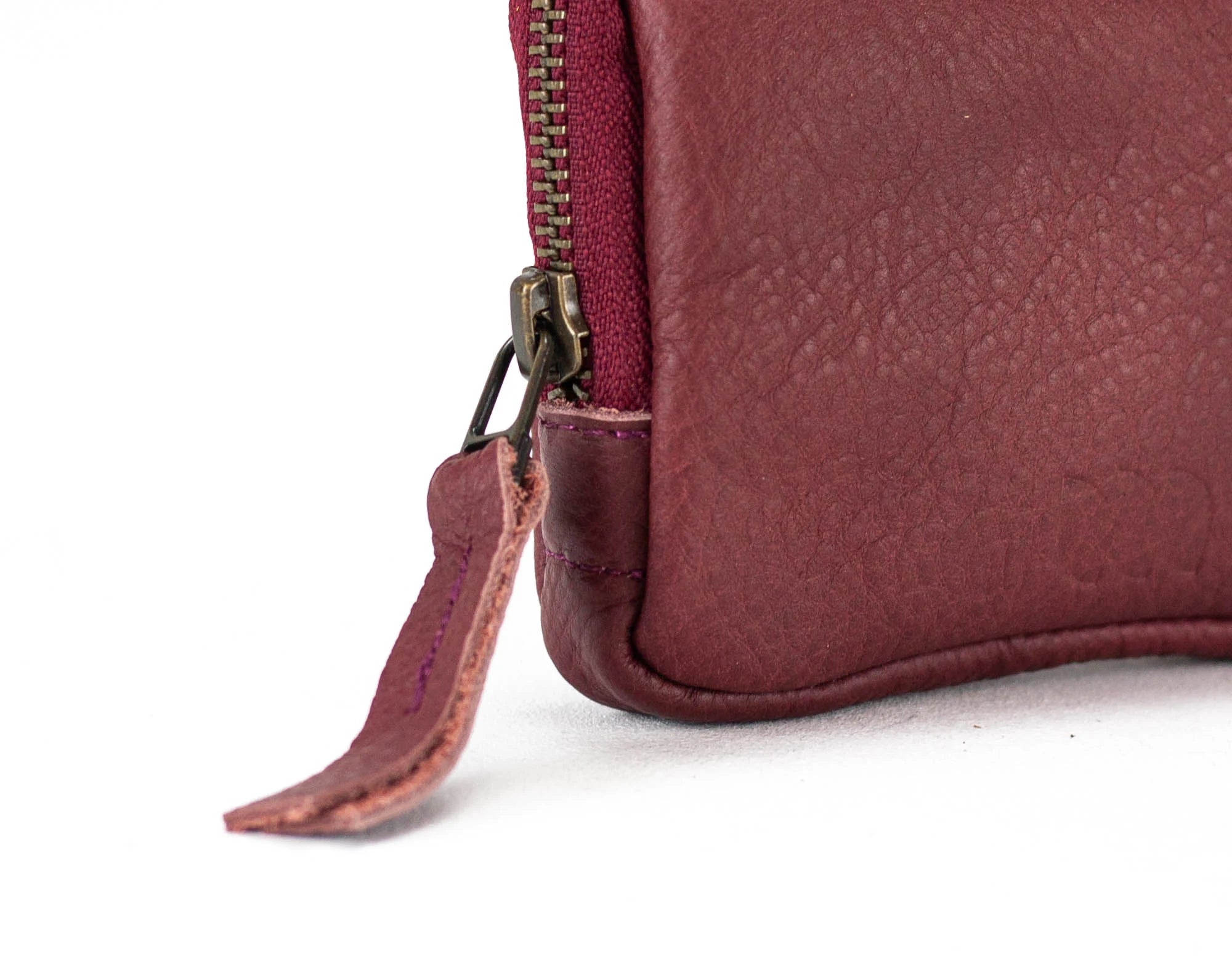 Close-up of a maroon leather pouch with a zipper on a white background