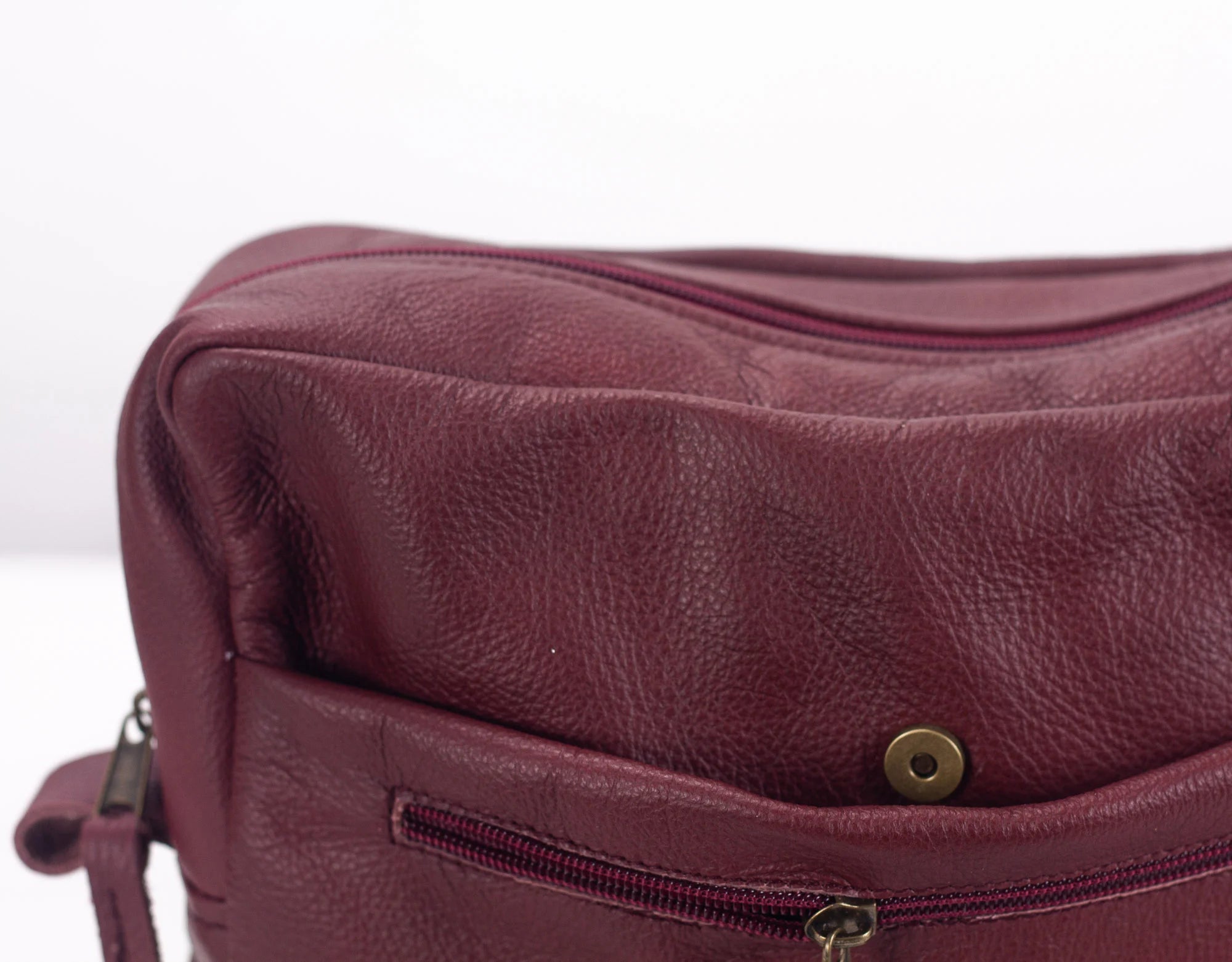 Close-up of a maroon leather bag with a zipper on a white background