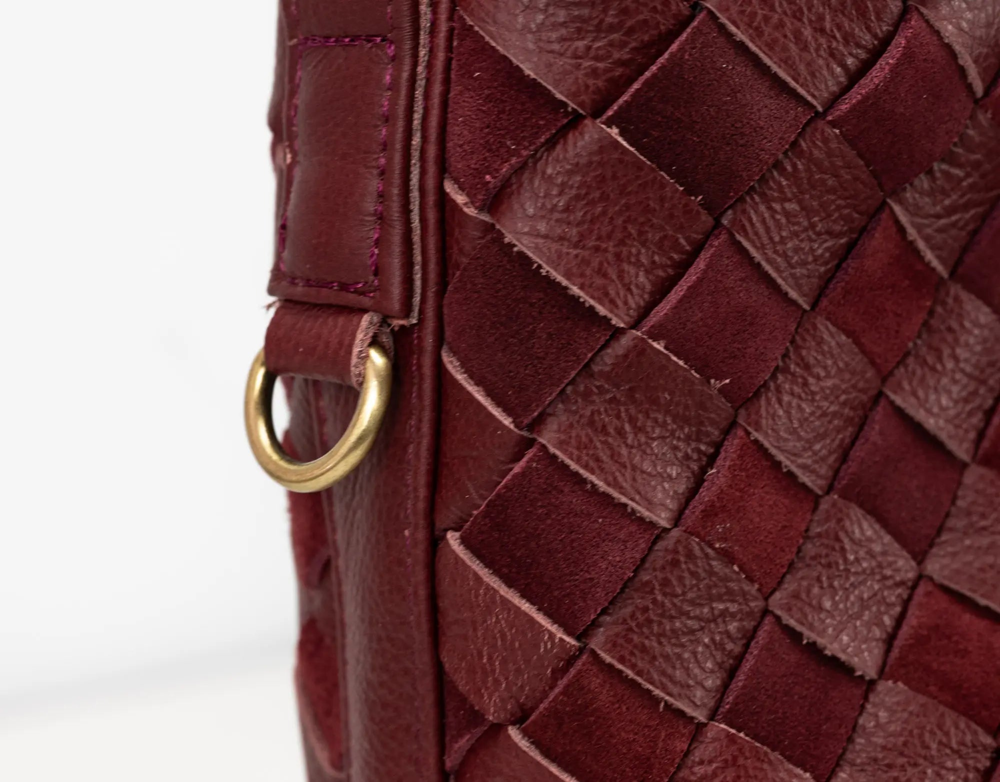 Close-up of a maroon woven leather handbag with a gold ring handle.