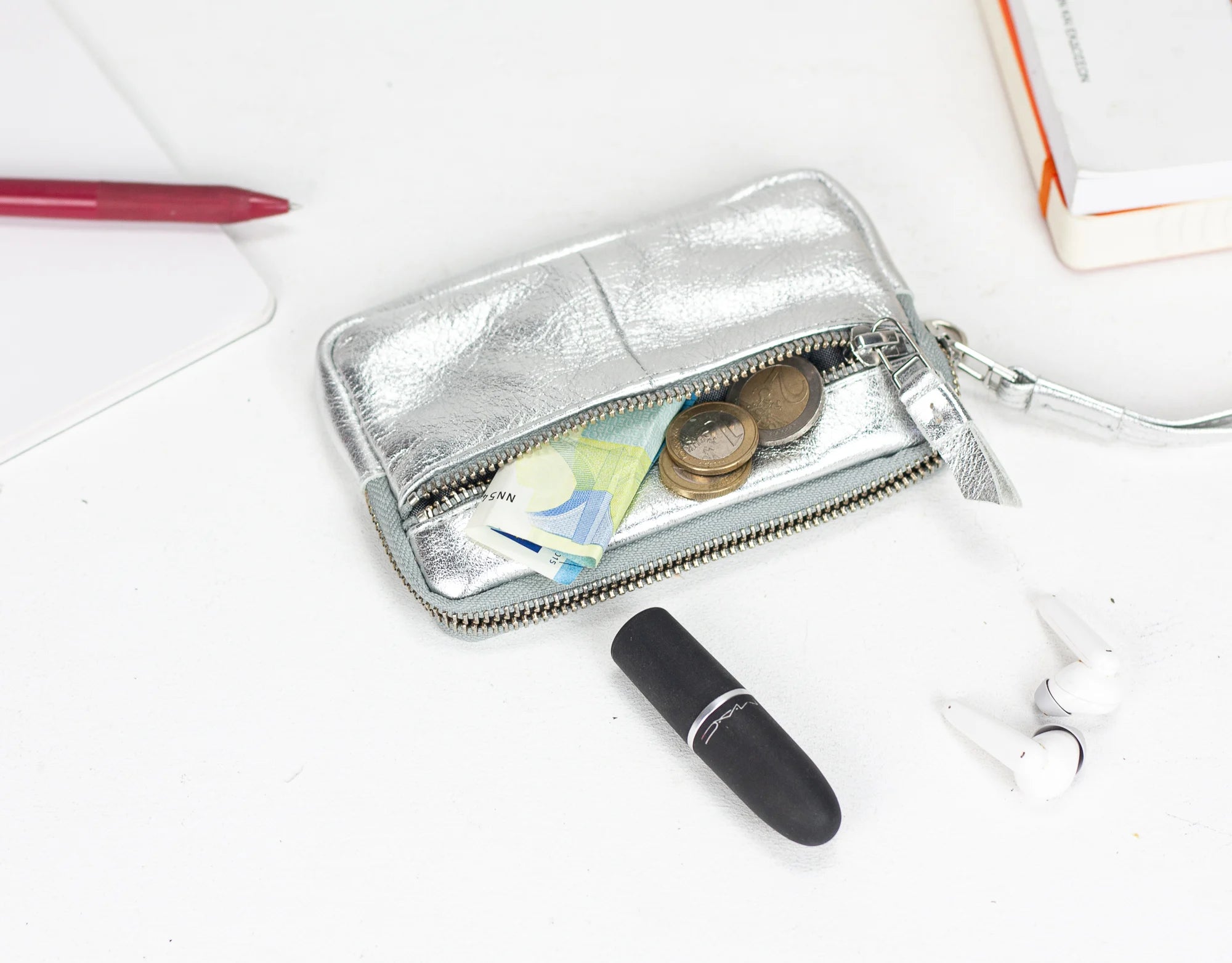 Silver wallet with coins, cards, and a lipstick on a white surface