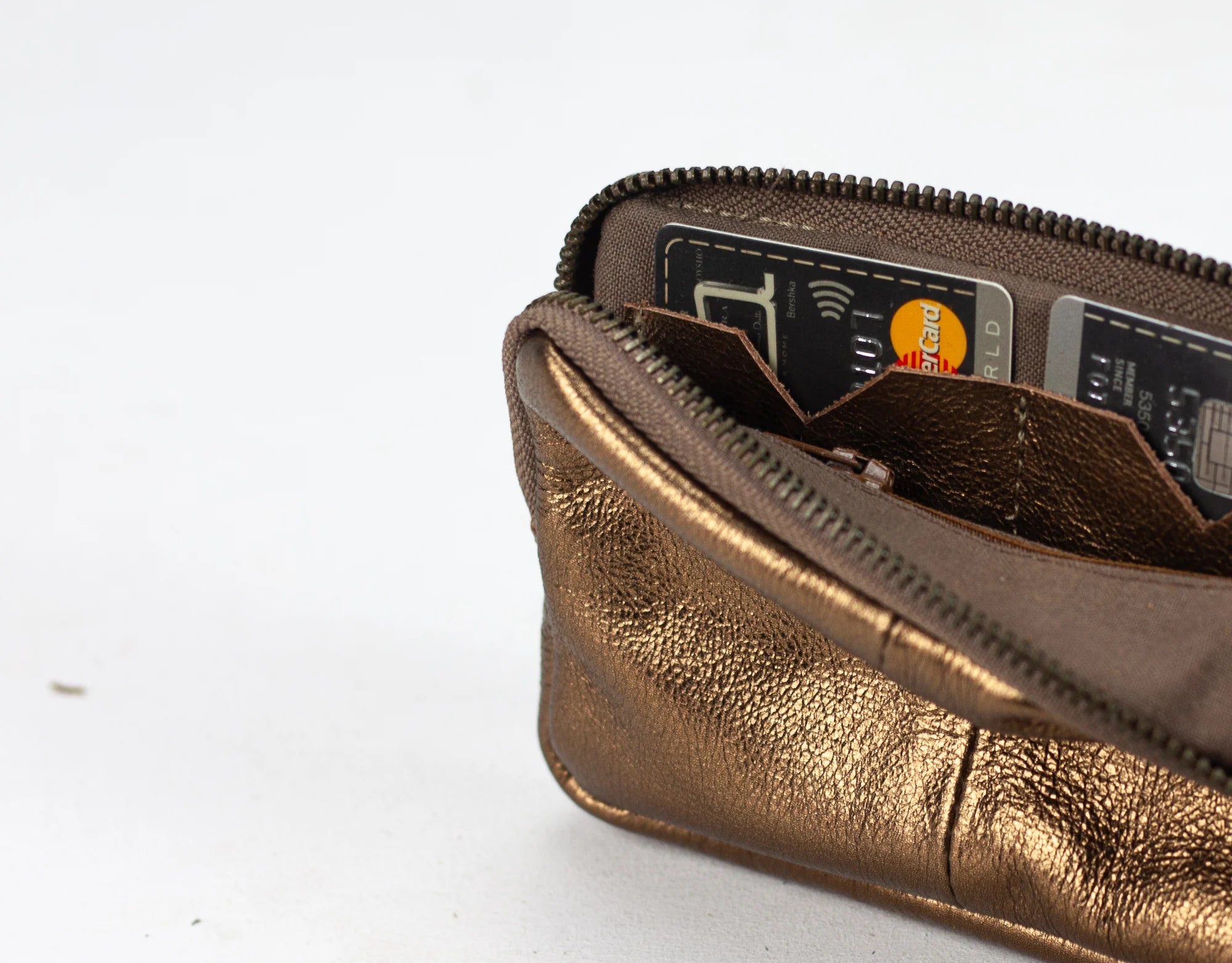 Bronze-colored wallet with a zipper, containing cards on a white background