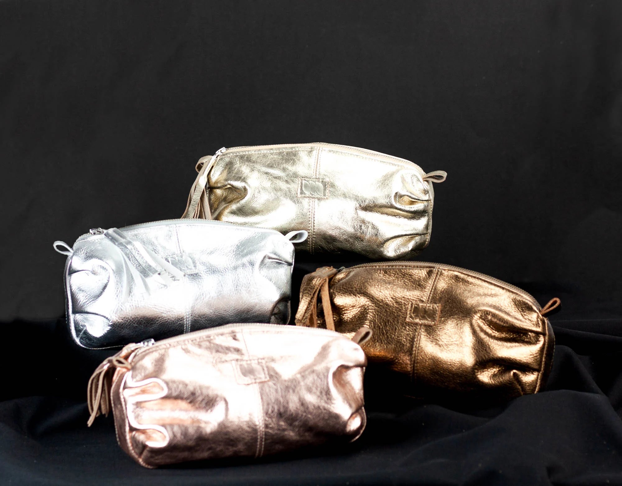 Four metallic pouches in silver, gold, and bronze on a black background