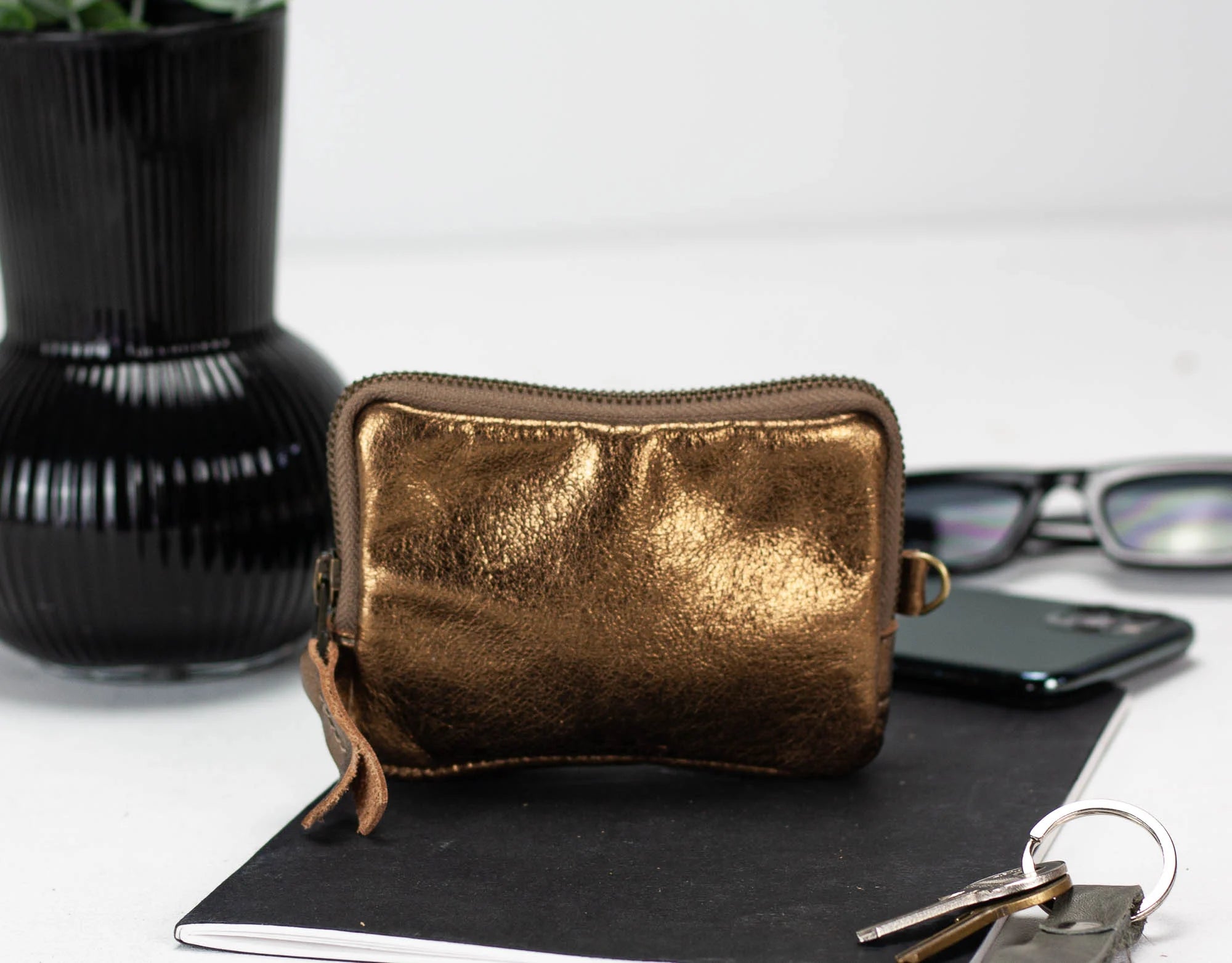 Gold metallic pouch on a notebook with a black vase and glasses in the background