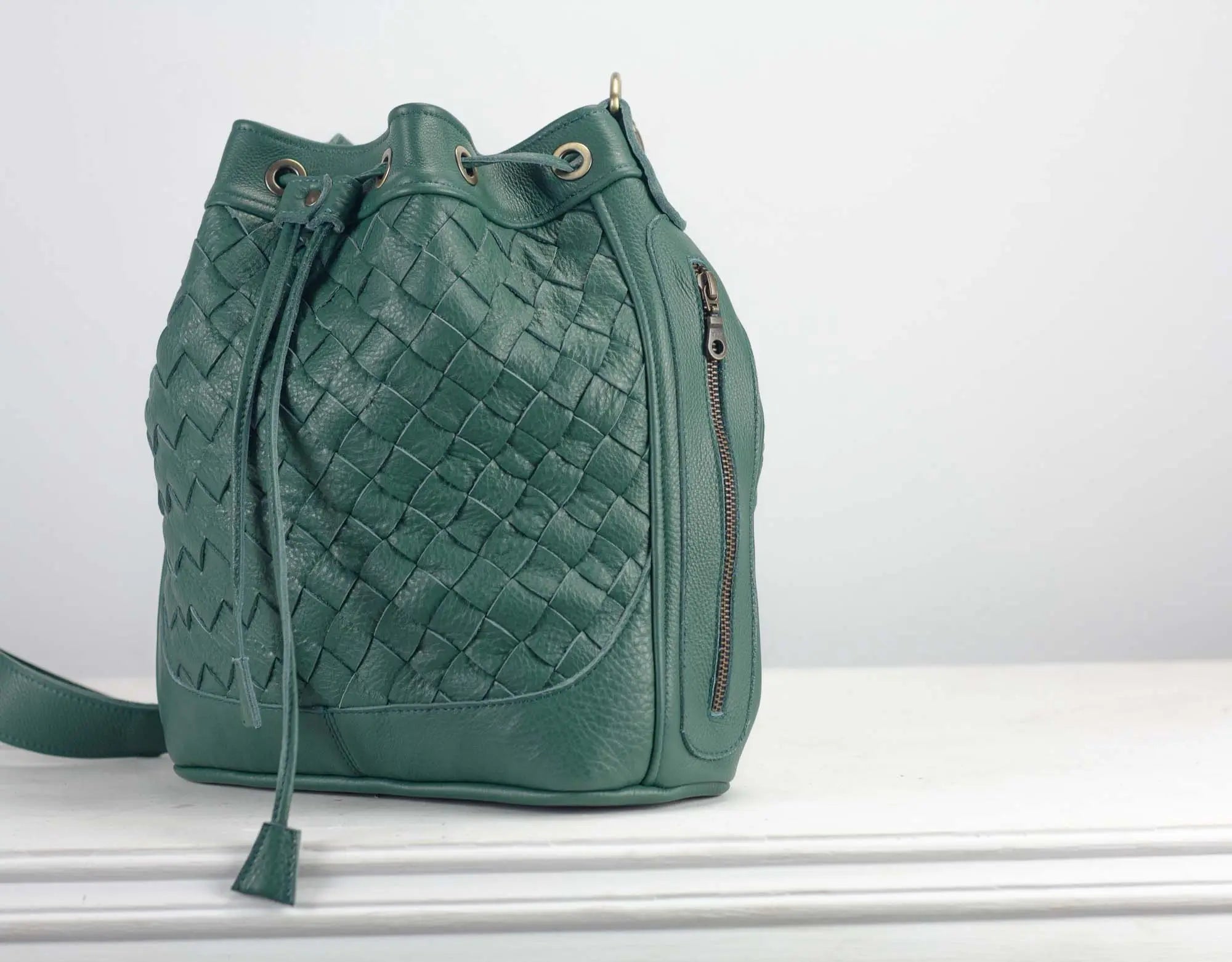Green woven leather bag on a white surface with a light gray background