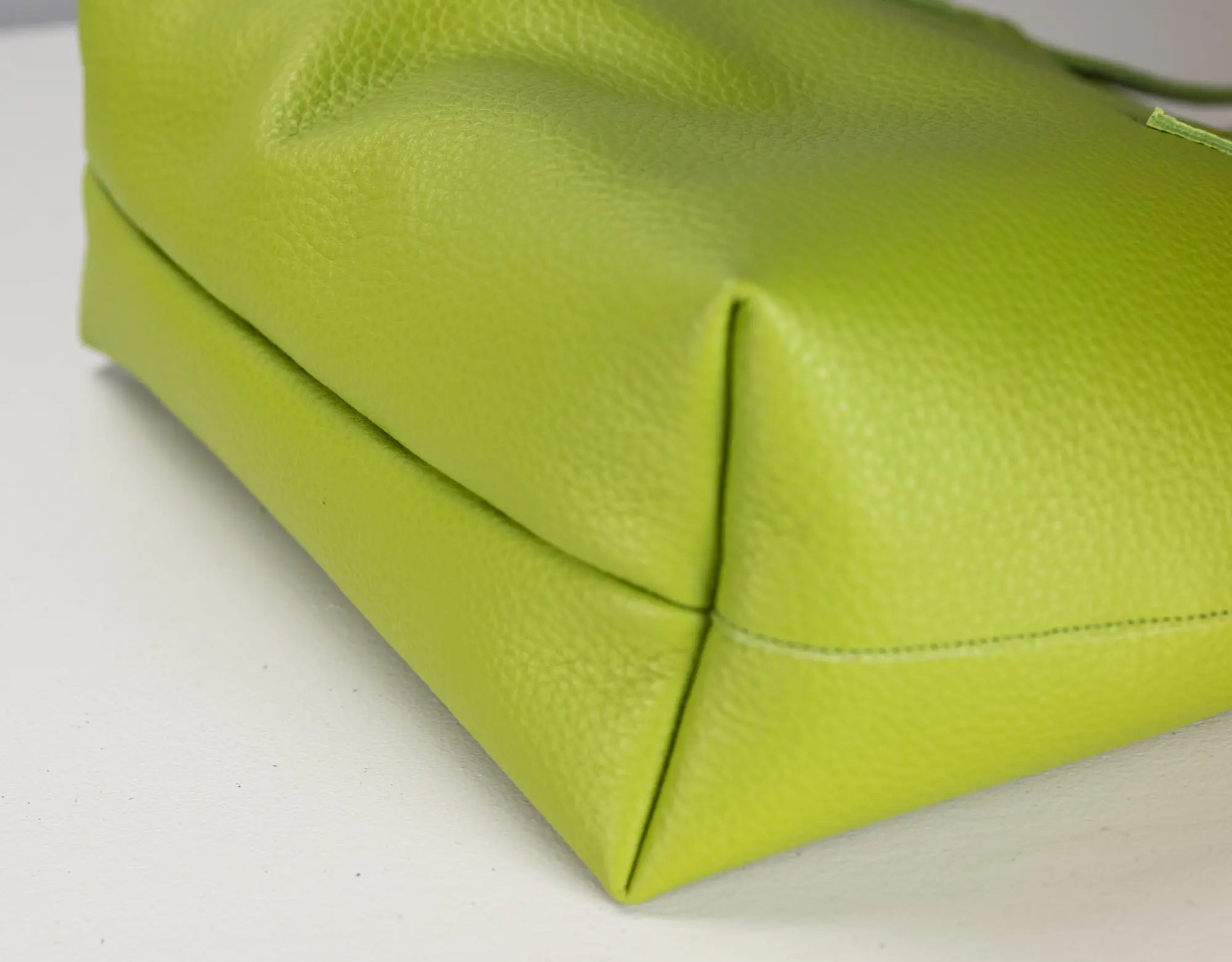 Close-up of a bright lime green pebbled leather handbag corner on a white surface.