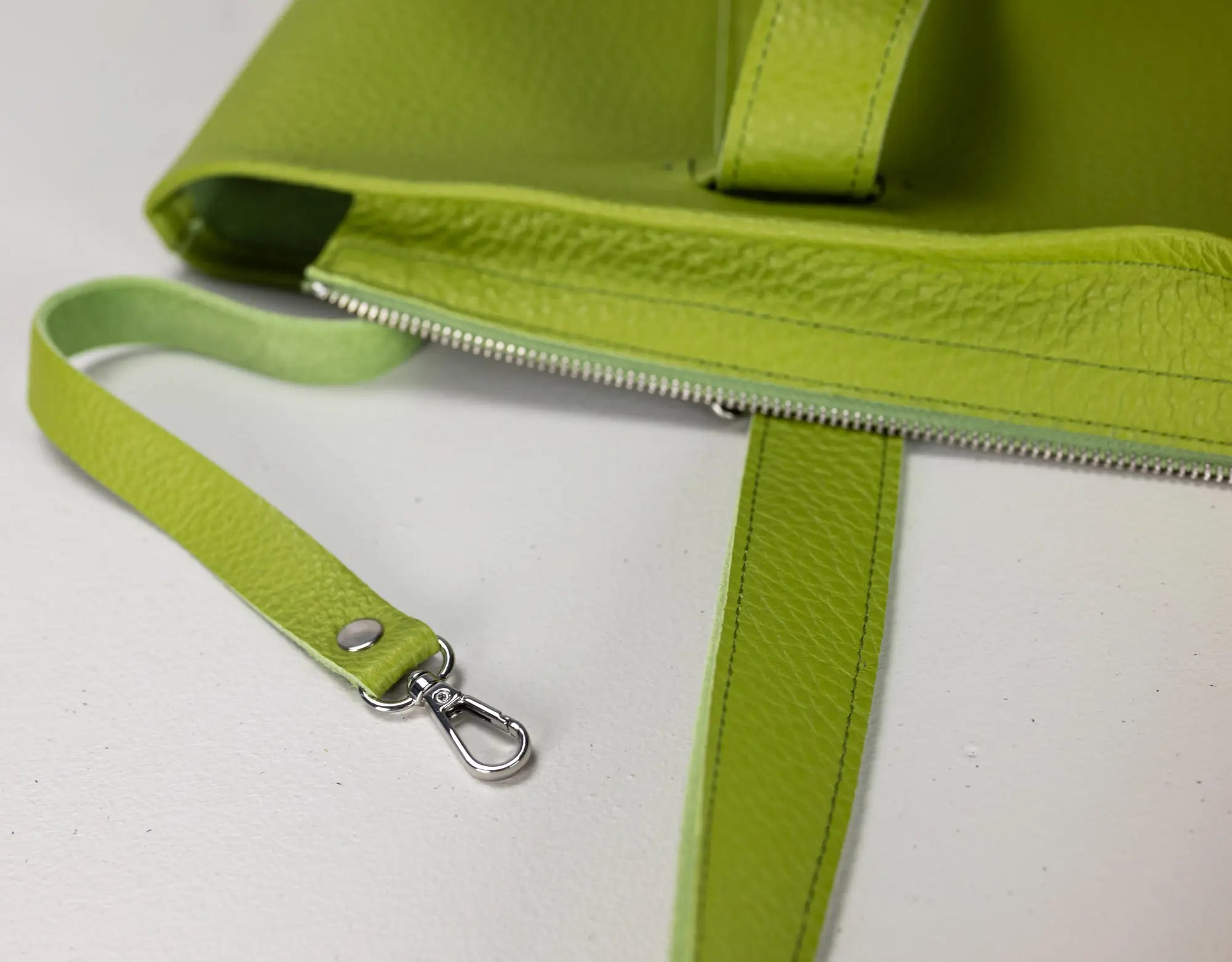 Close-up of a bright lime green pebbled leather bag with a matching wristlet strap and silver-tone metal clasp, shown on a white surface.