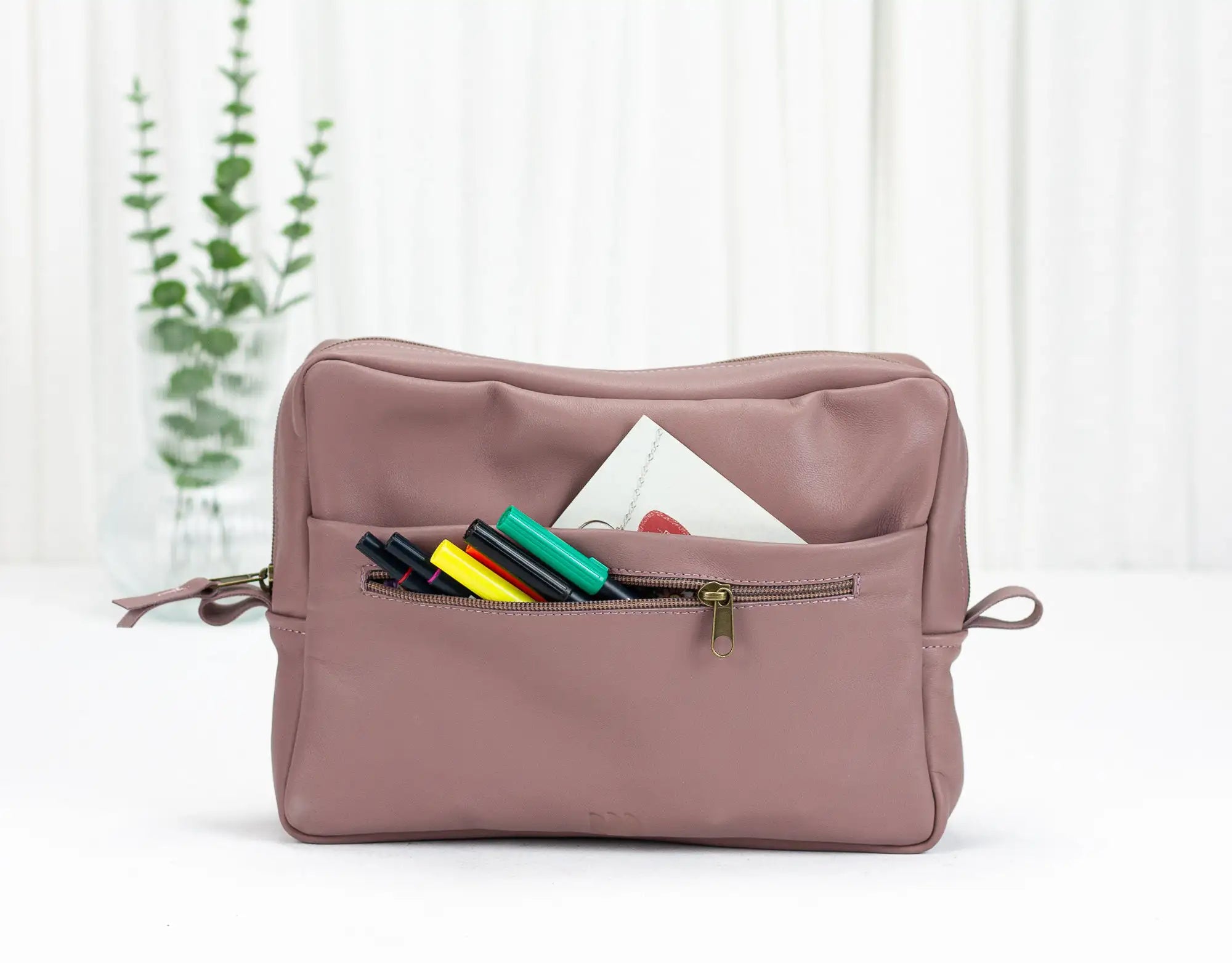 Pink toiletry bag with colorful items on a white background