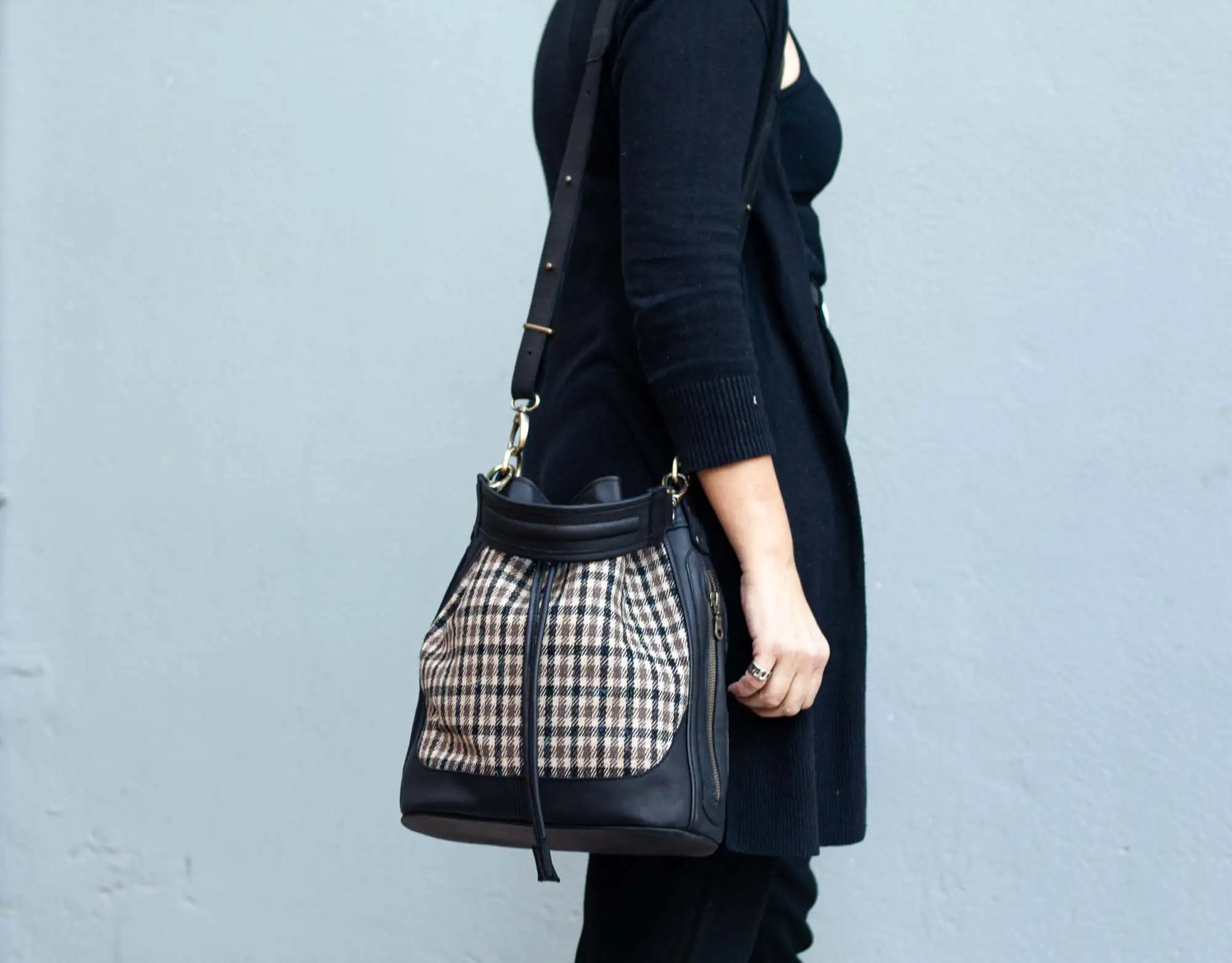 Person holding a black handbag with plaid pattern against a light blue background