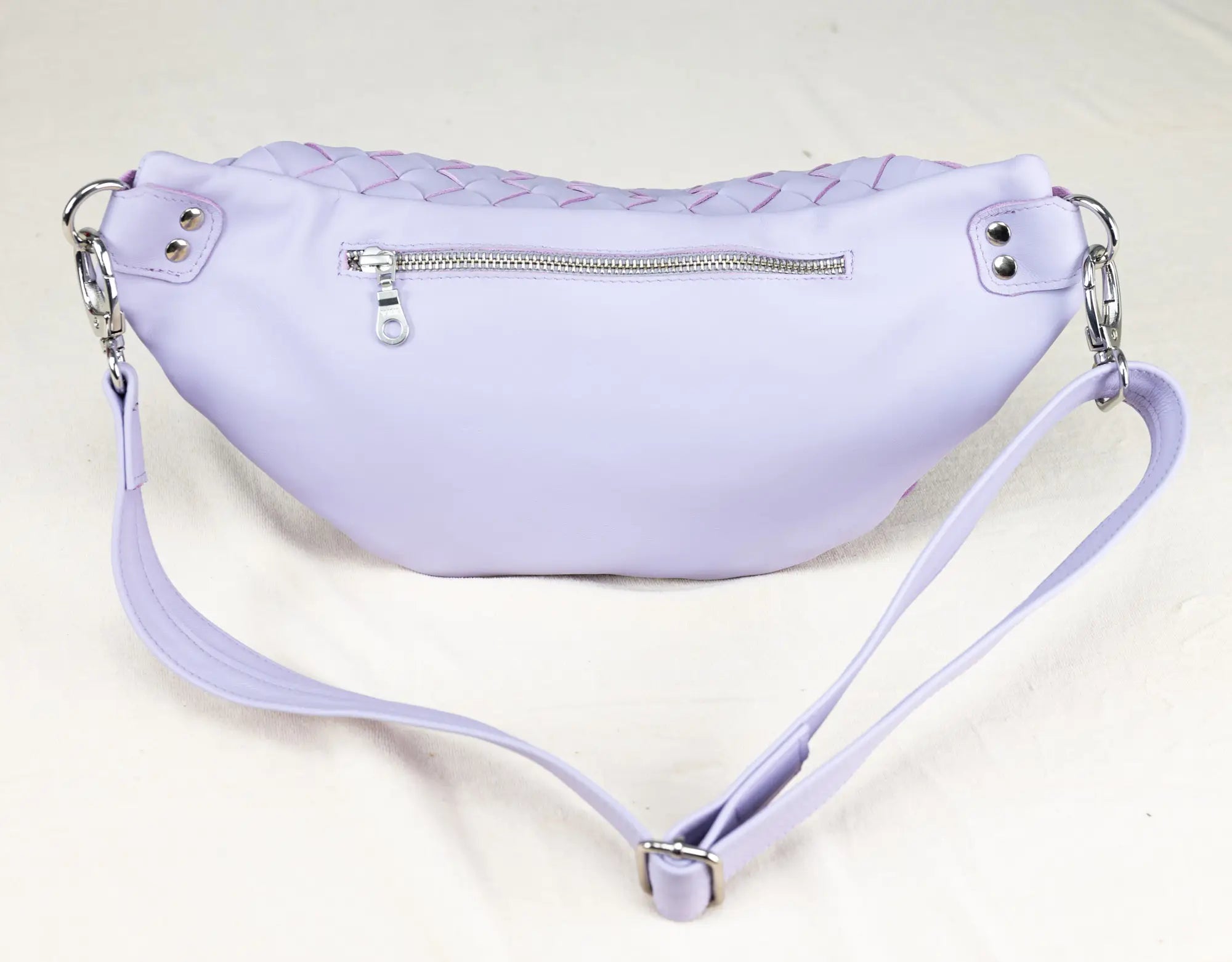 Lavender waist bag with braided top and zippers on a light gray background
