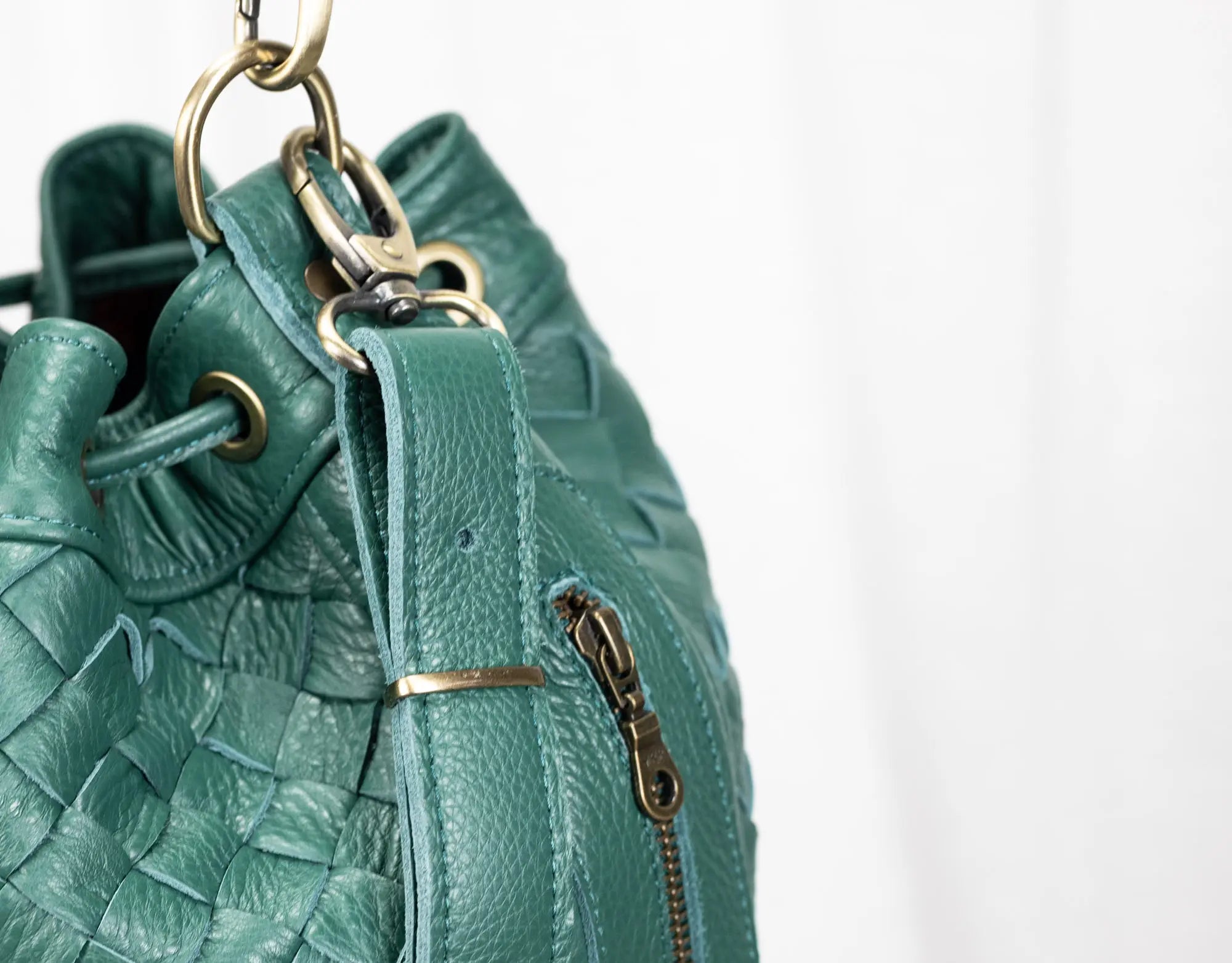 Teal leather handbag with braided design and gold zipper on a white background