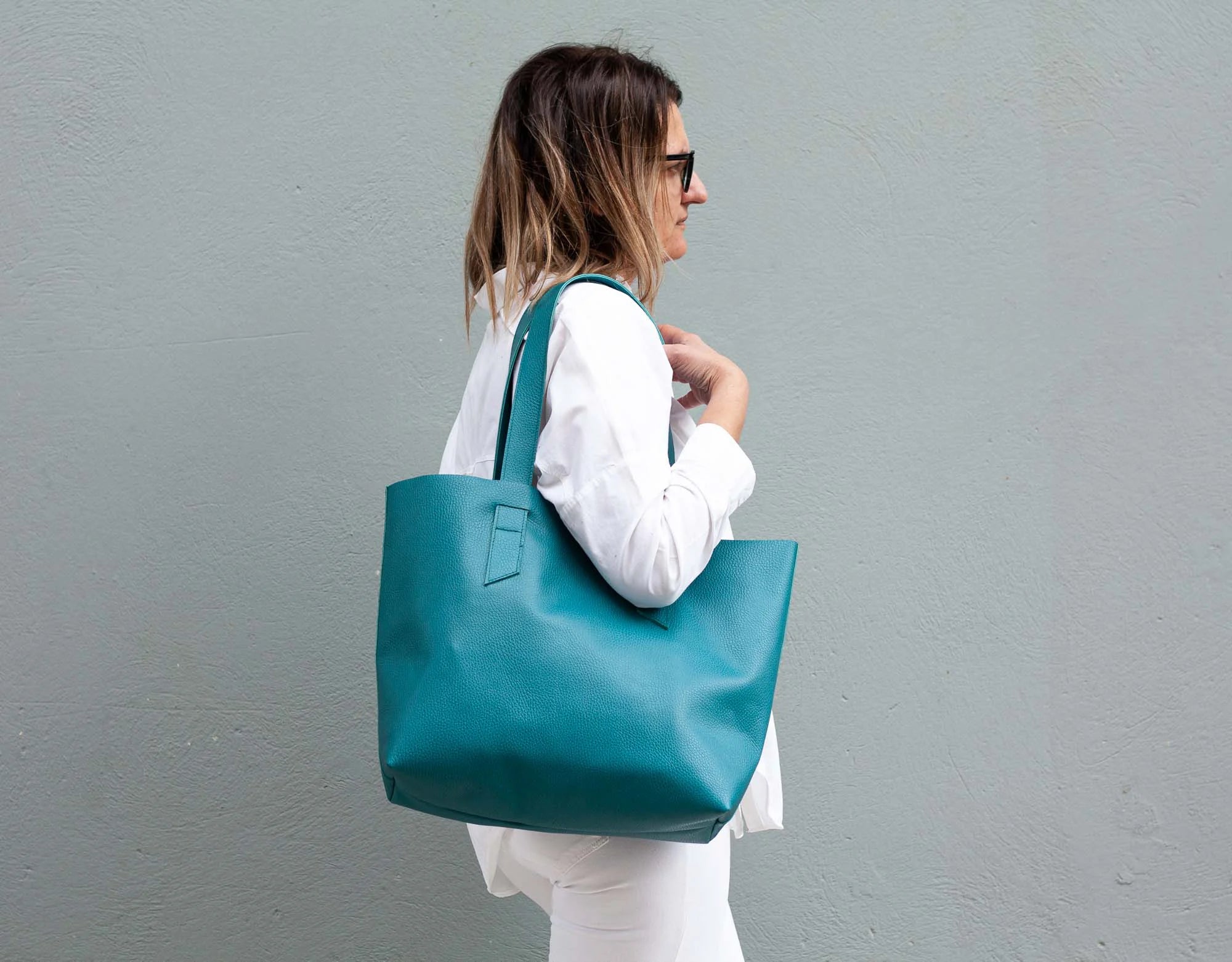 Woman holding a teal tote bag against a gray background