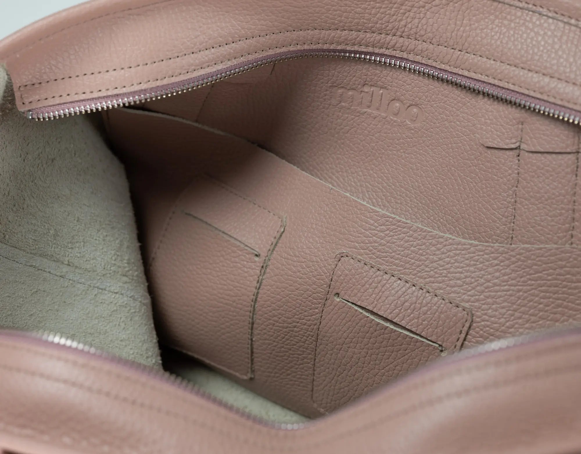 Close-up of the interior of a blush pink pebbled leather bag, showing a zippered compartment, interior pocket, and the embossed brand name &