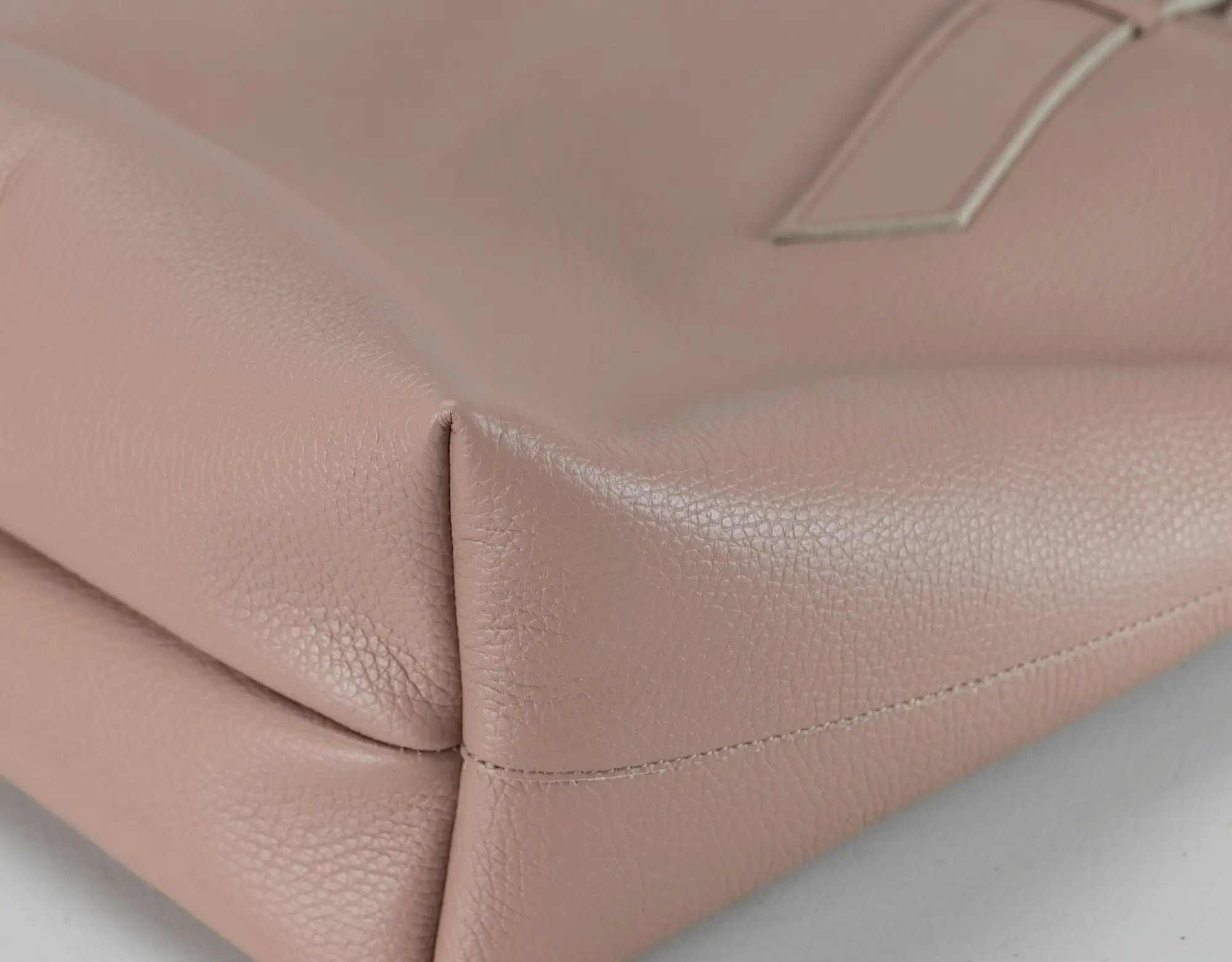 Close-up of a blush pink pebbled leather handbag corner showing the texture and stitching detail.