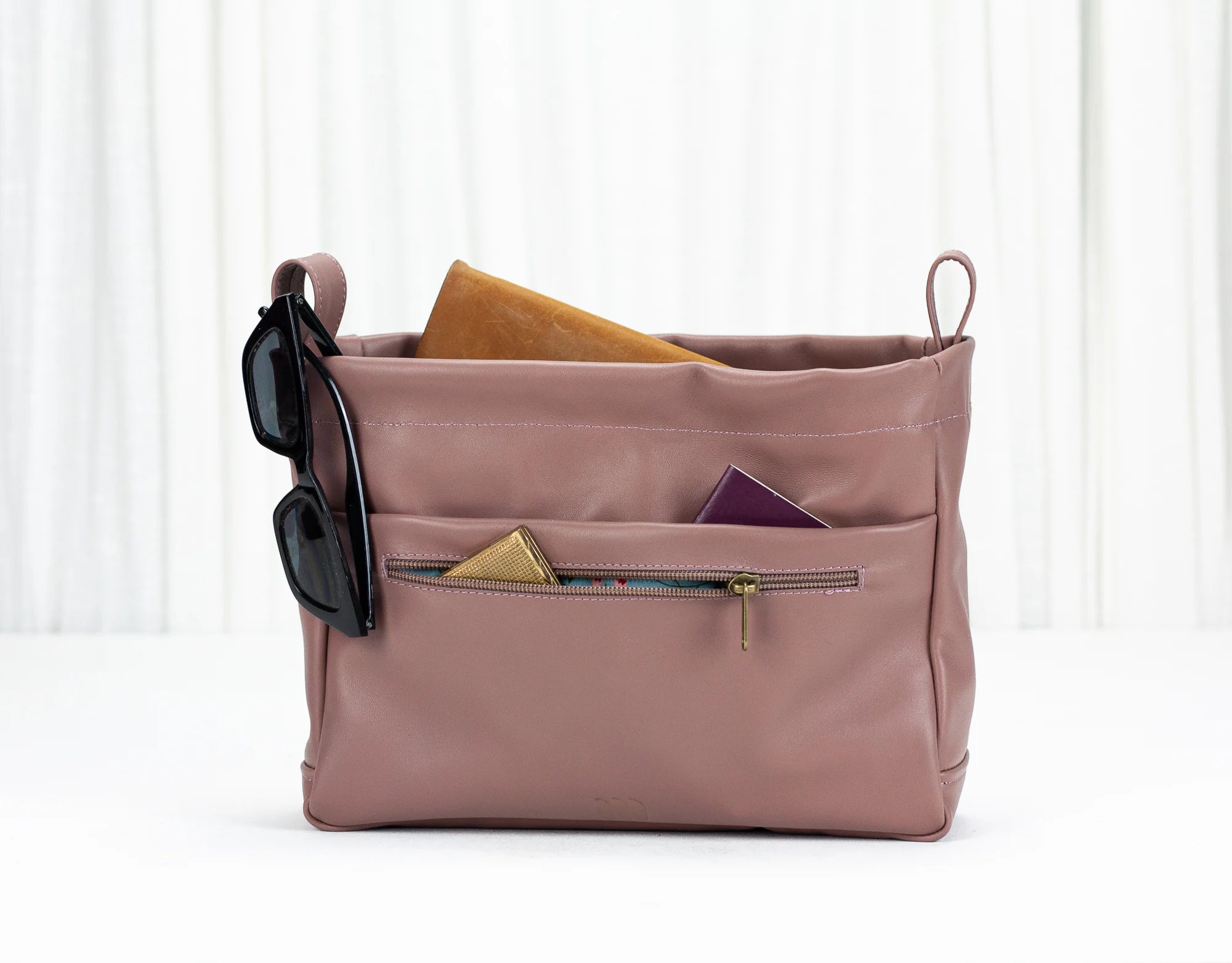 Pink bag with sunglasses and a phone inside on a white background