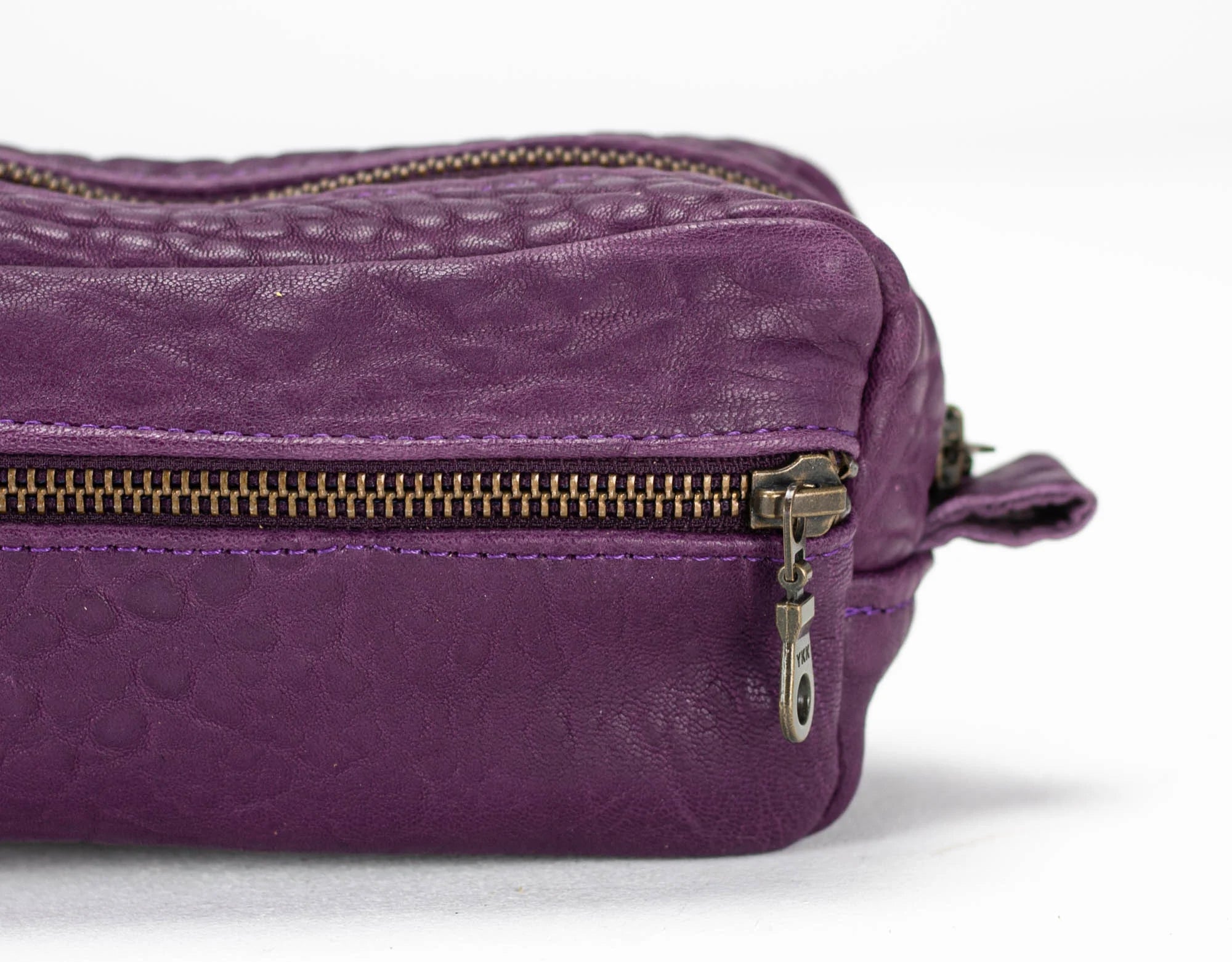 Purple leather bag with gold zipper on a white background