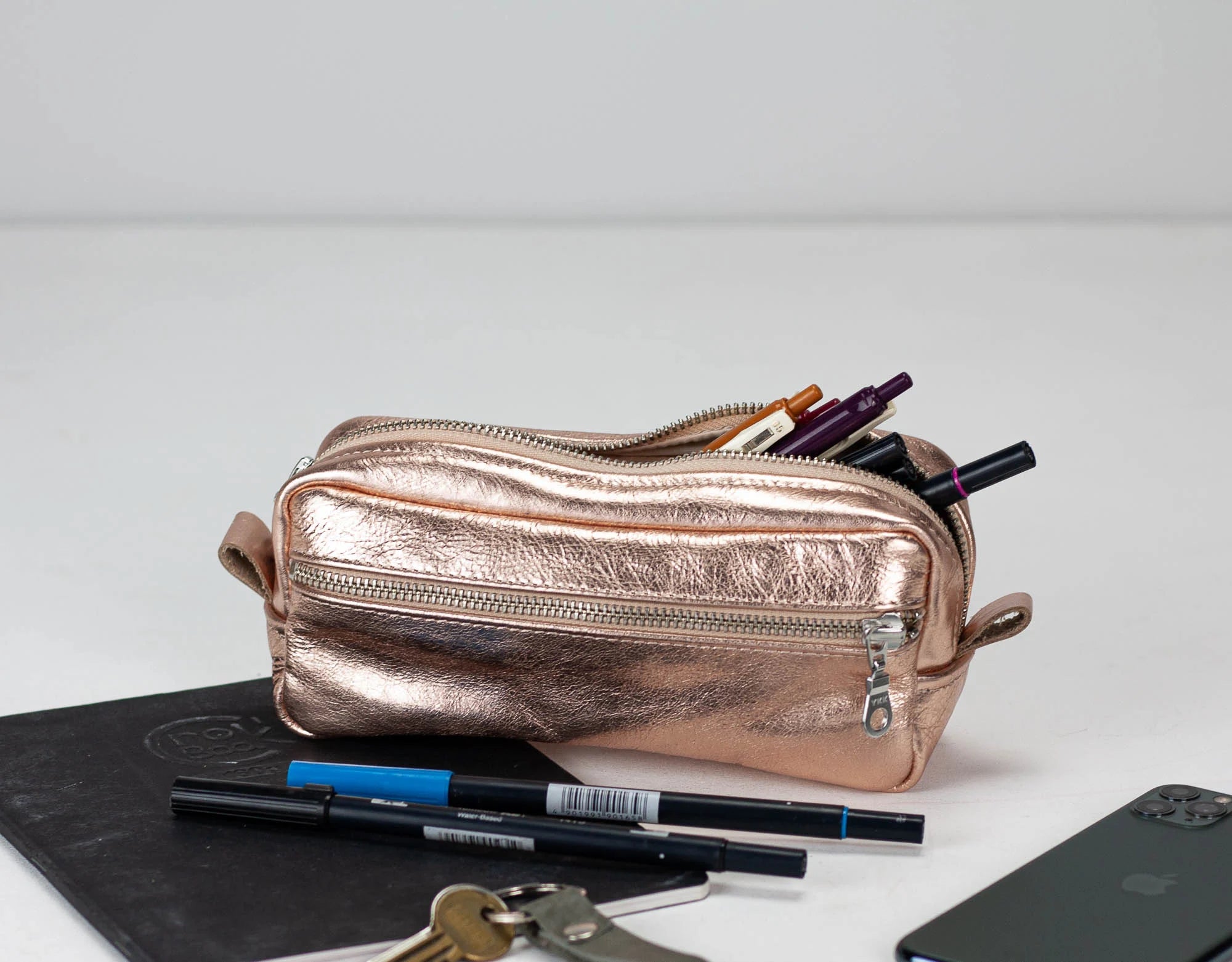 Rose gold pencil case with stationery items on a white surface