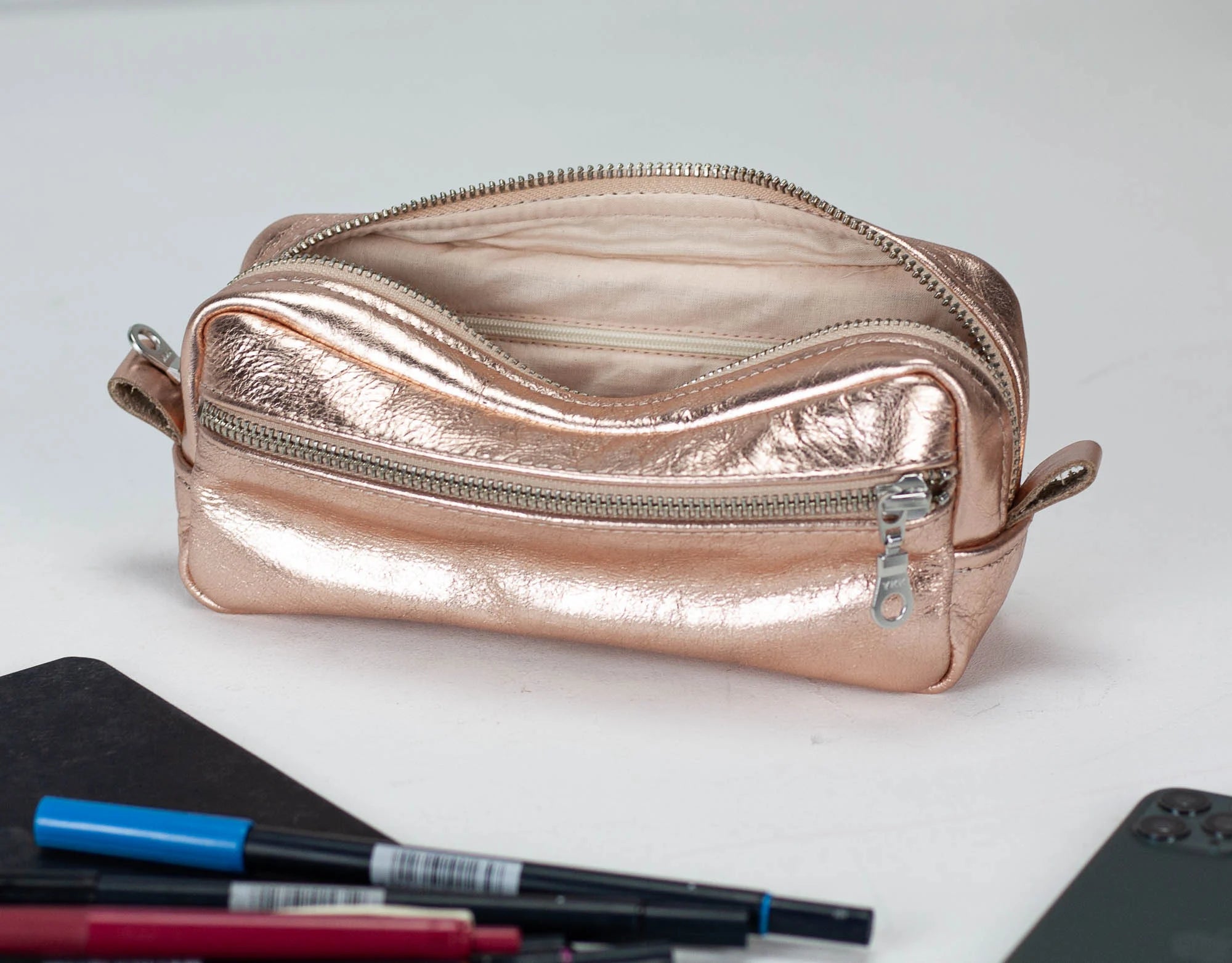Rose gold metallic pouch on a white surface with stationery items.