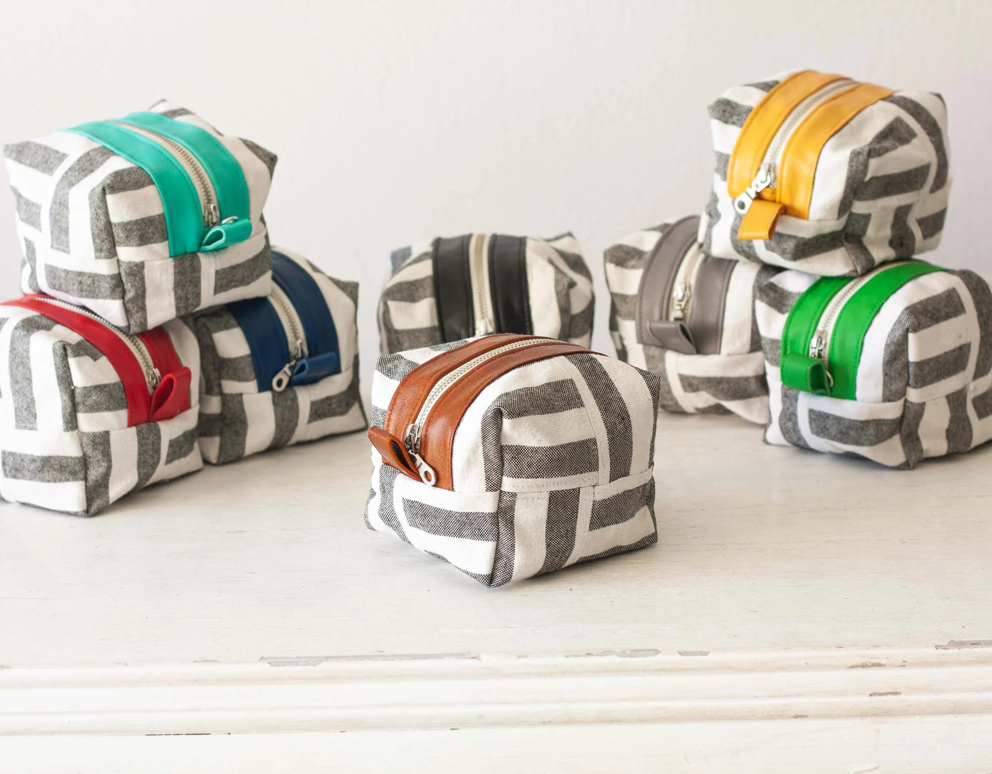 Set of fabric pouches with geometric patterns and colorful zippers on a white surface.