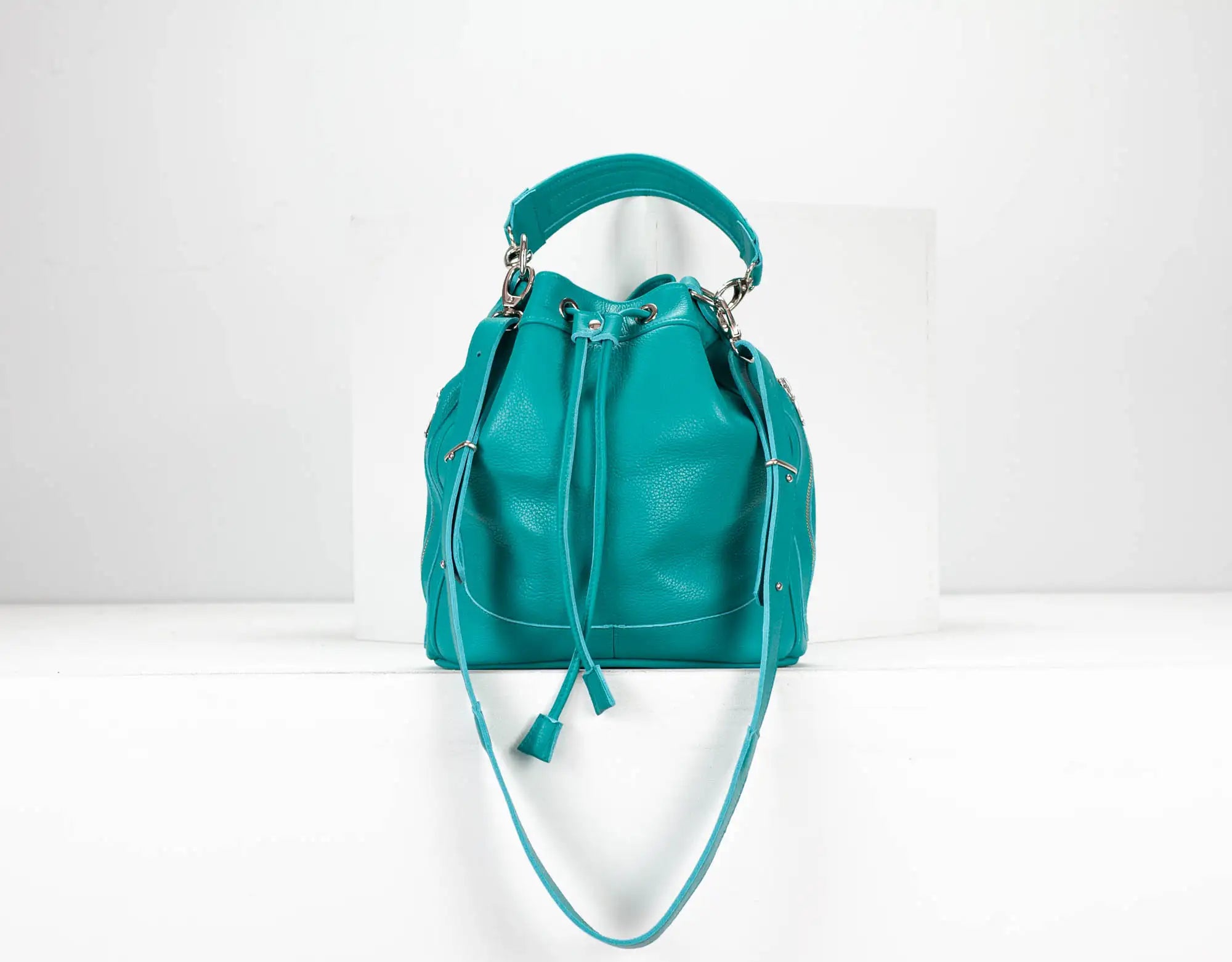 Teal leather handbag with drawstring on a white background