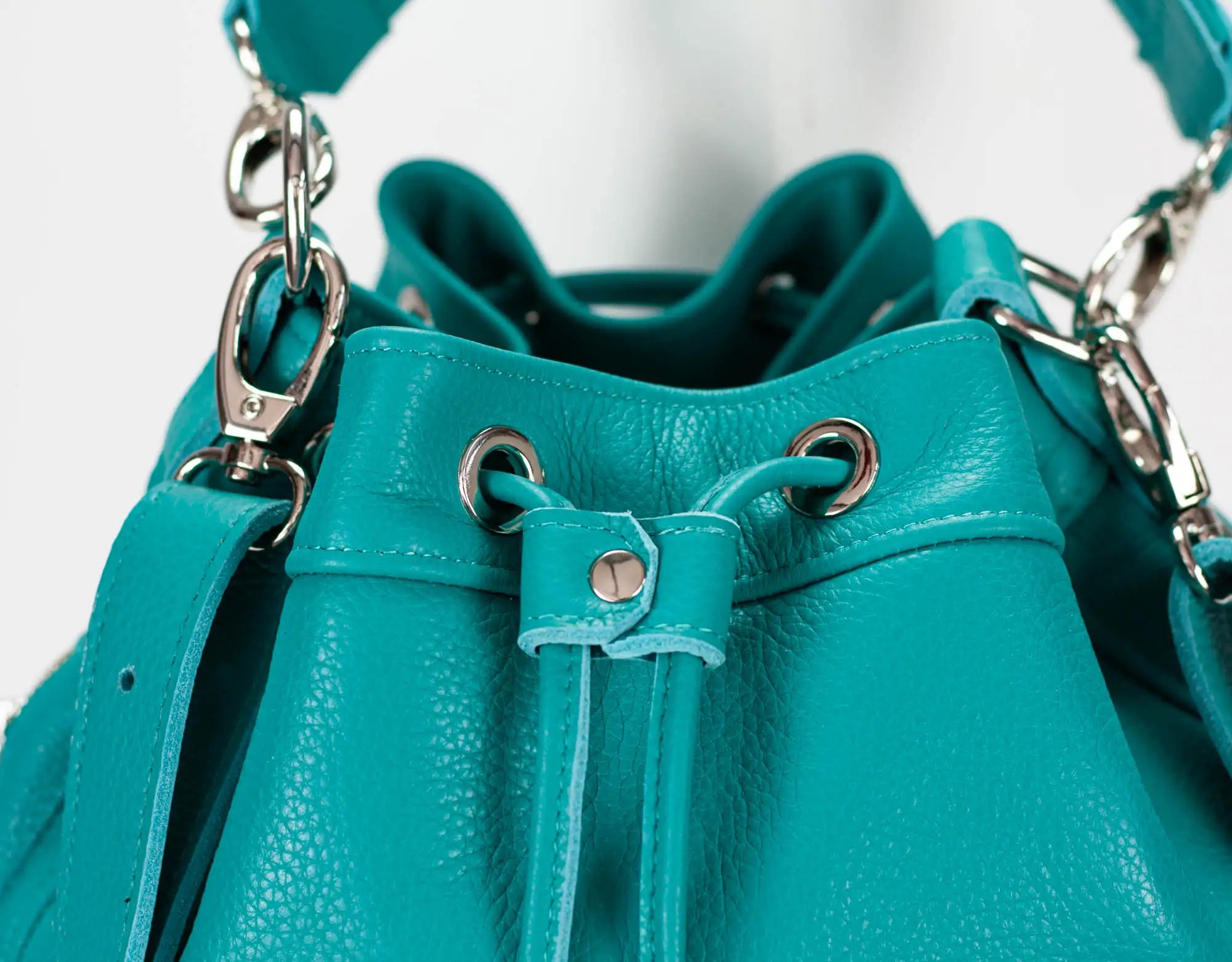 Teal leather handbag with drawstring closure on a white background