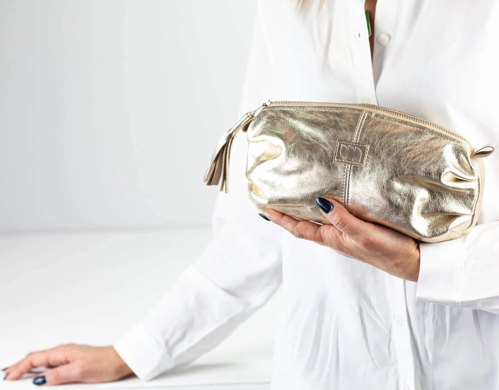 Gold clutch bag held by a person wearing a white outfit on a light gray background
