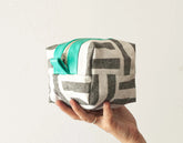 Hand holding a small fabric pouch with a geometric pattern and turquoise zipper on a light background