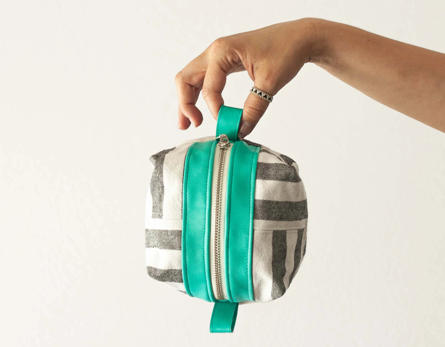Hand holding a striped pouch with a green zipper against a plain background