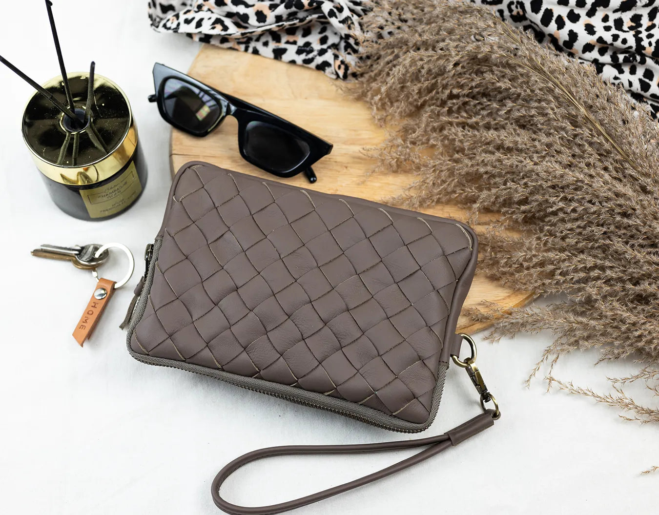 Brown quilted clutch bag on a white surface with sunglasses and other accessories.