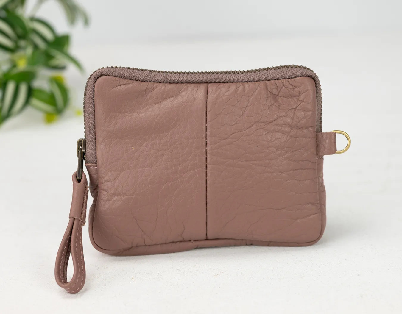 old rose leather clutch bag on a white background with a plant in the corner