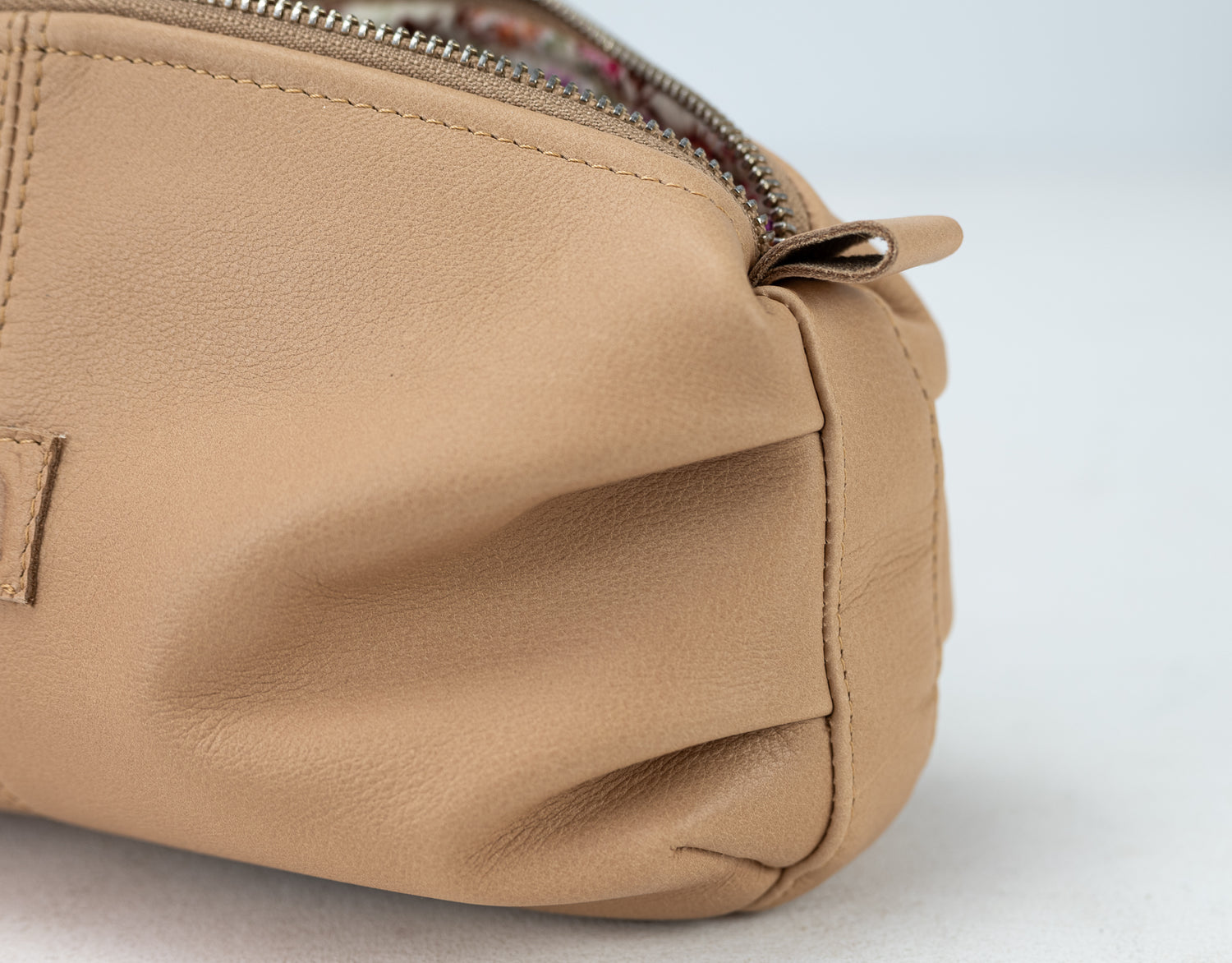 Close-up of a beige leather bag with a zipper on a light gray background
