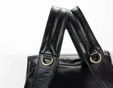 Black leather bag with gold hardware straps on a white background