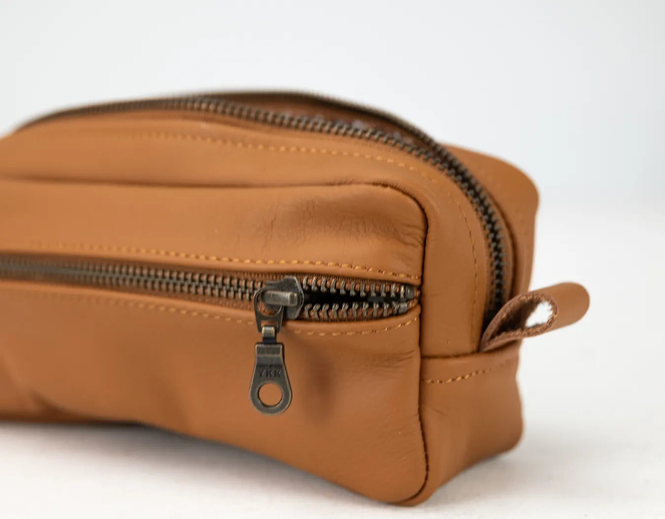 Brown leather toiletry bag with a zipper on a white background