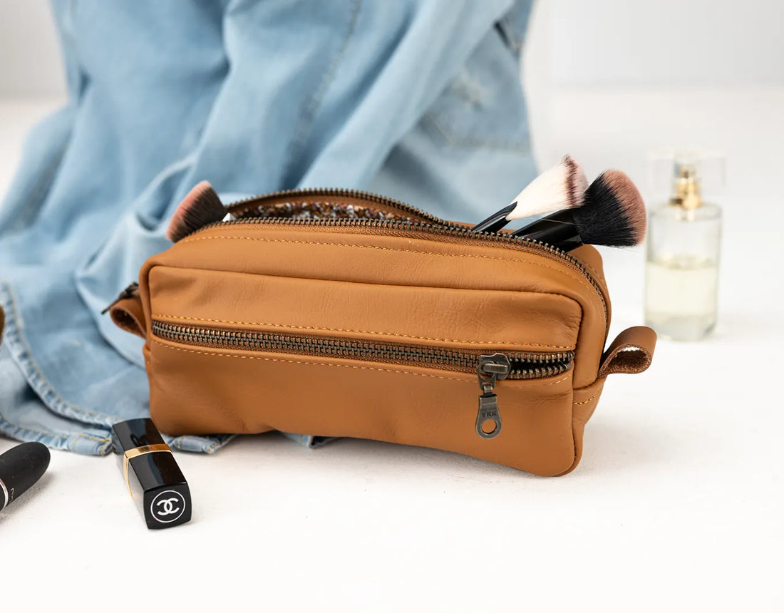 Brown leather toiletry bag with makeup items on a light background