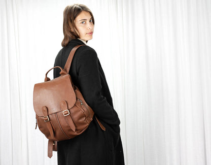 Woman wearing a brown leather backpack against a white curtain background