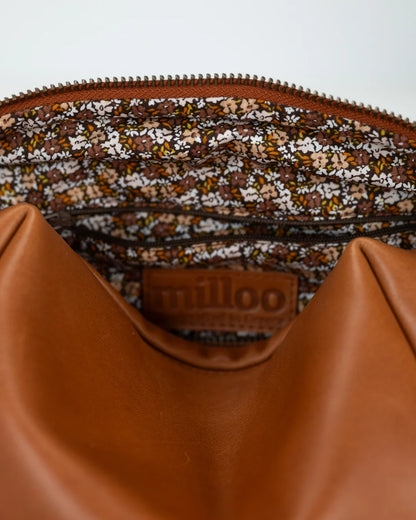 Close-up of a brown leather bag with a floral patterned interior lining, featuring the brand &