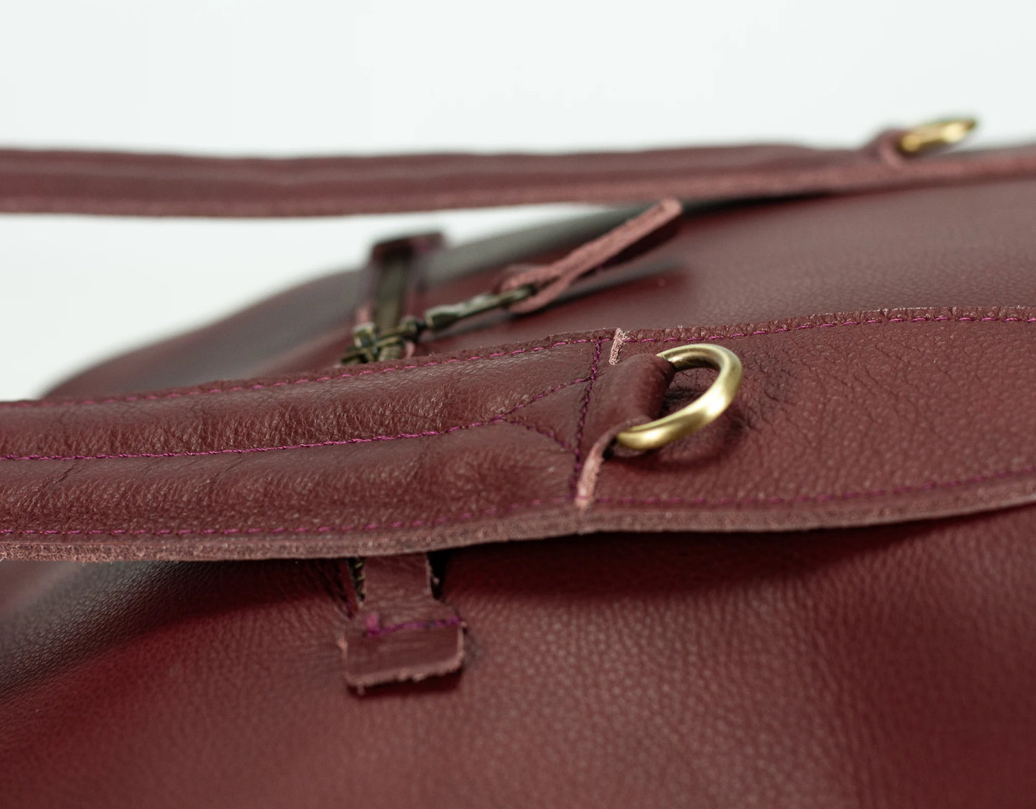 Close-up of a maroon leather bag with gold hardware on a white background