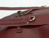 Close-up of a maroon leather bag with gold hardware on a white background