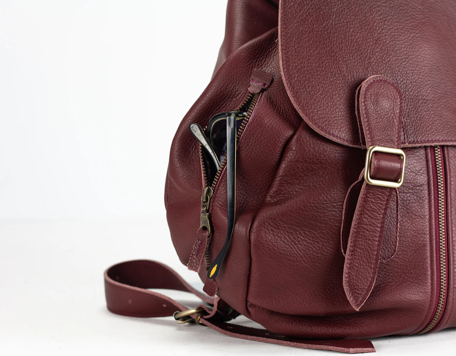 Close-up of a maroon leather backpack with gold buckle on a white background