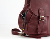 Close-up of a maroon leather backpack with gold buckle on a white background